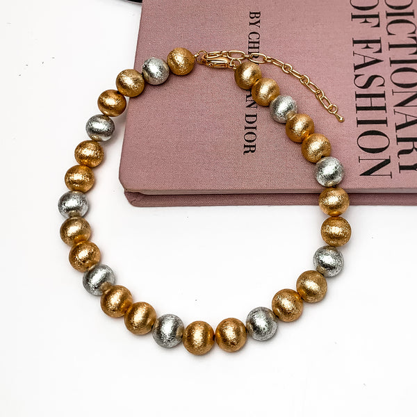 Medium mixed metals beaded necklace. Shiny gold and silver coloring. This necklace is on a pink book with a white background.