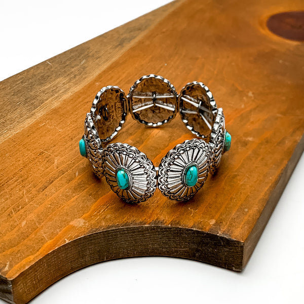 Western Concho Bracelet with Turquoise Center Stones in Silver Tone. This bracelet is pictured sitting on a wood piece. The background behind the wood is white.