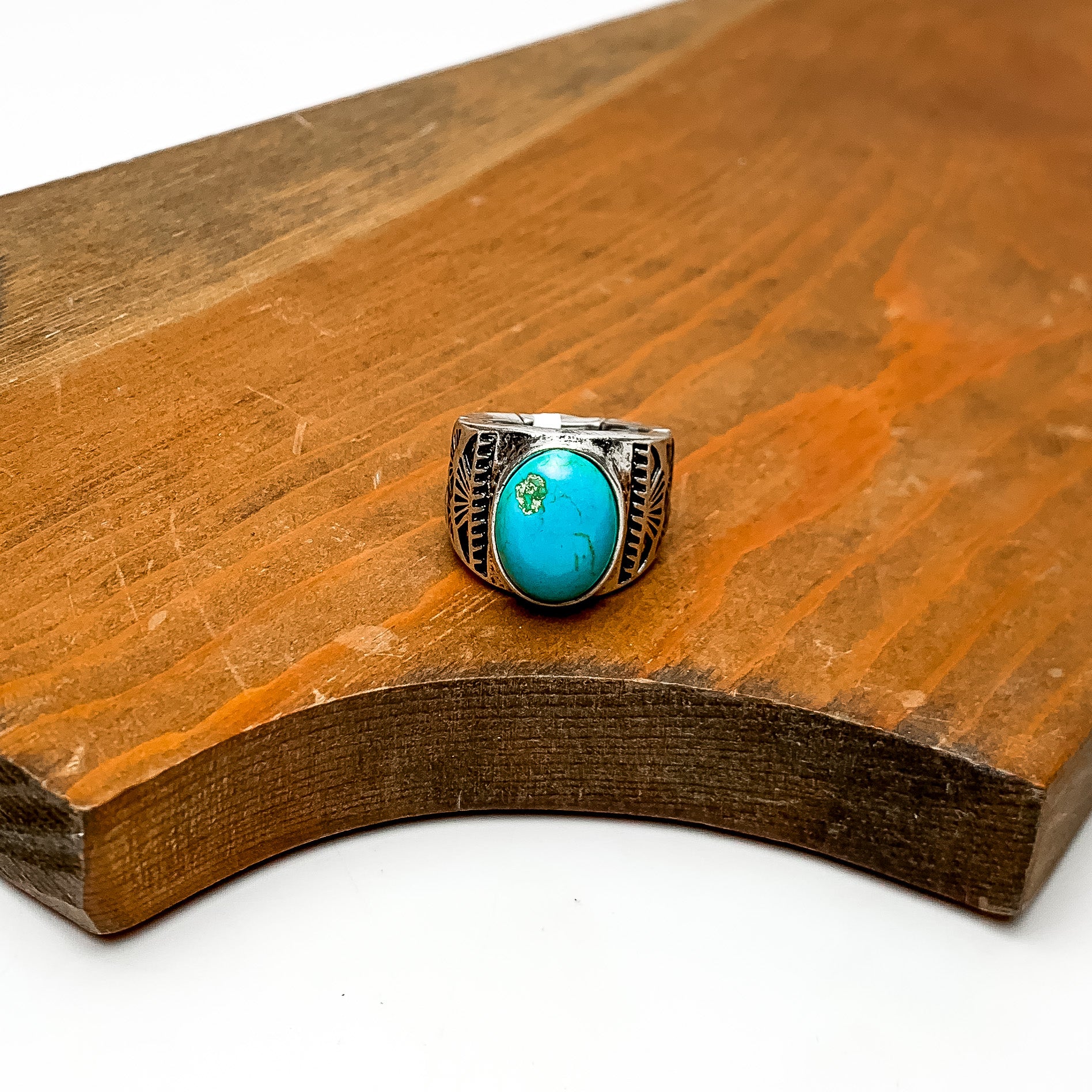 Faux Turquoise Stone Stretchy Ring With Silver Tone Design. This ring is pictured sitting on a wood piece. The background behind the wood is white.