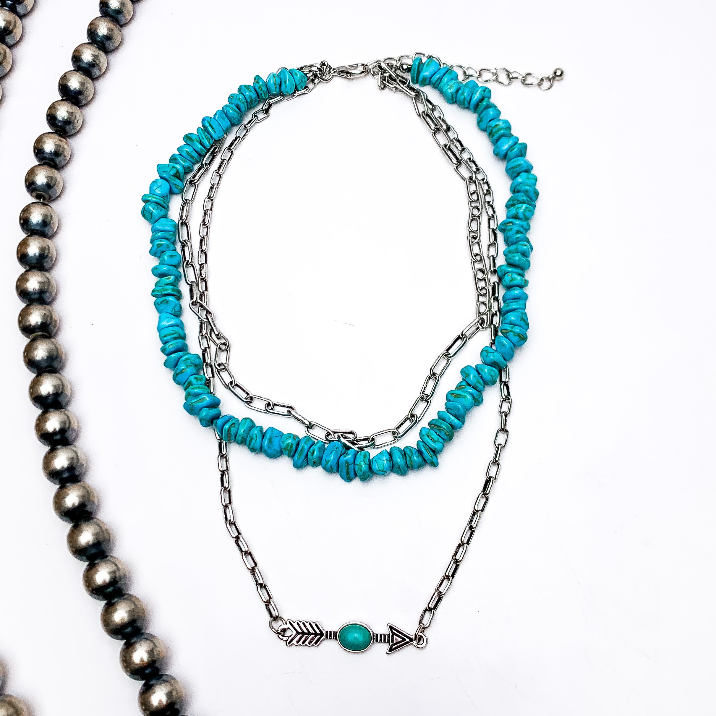 Triple Strand Silver Tone and Turquoise Necklace With an Arrow Charm. This necklace is on a white background with Navajo pearls on the left side for decoration.