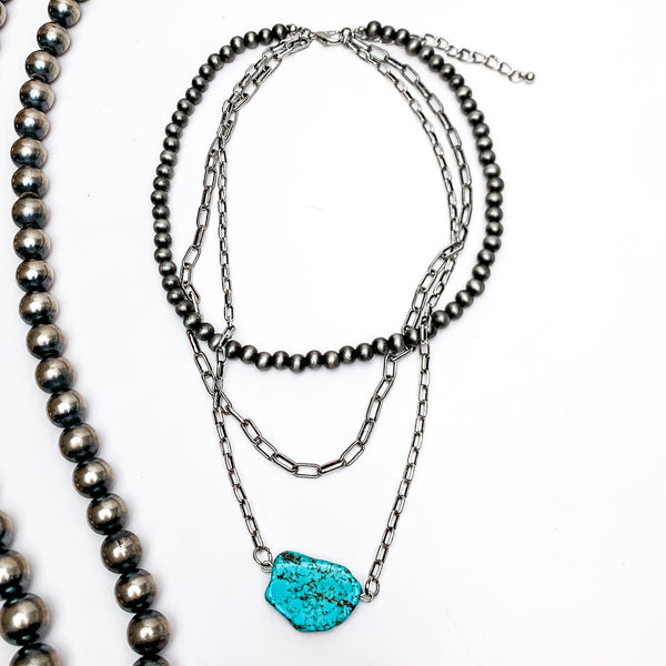 Triple Strand Silver Tone Necklace With Turquoise Stone . This necklace is on a white background with Navajo pearls on the left side for decoration.