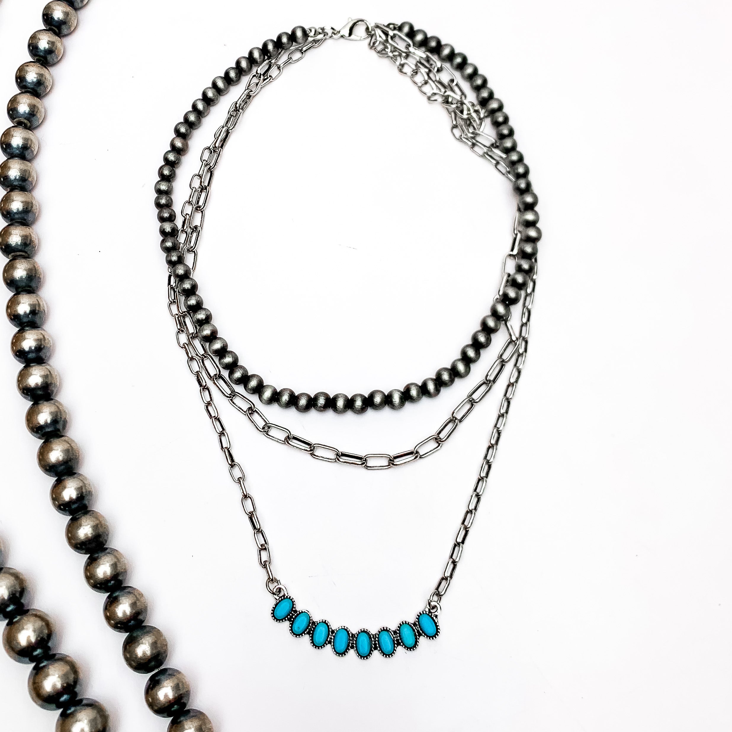 Triple Strand Silver Tone Necklace With Turquoise Stones Pendant. This necklace is on a white background with Navajo pearls on the left side for decoration.