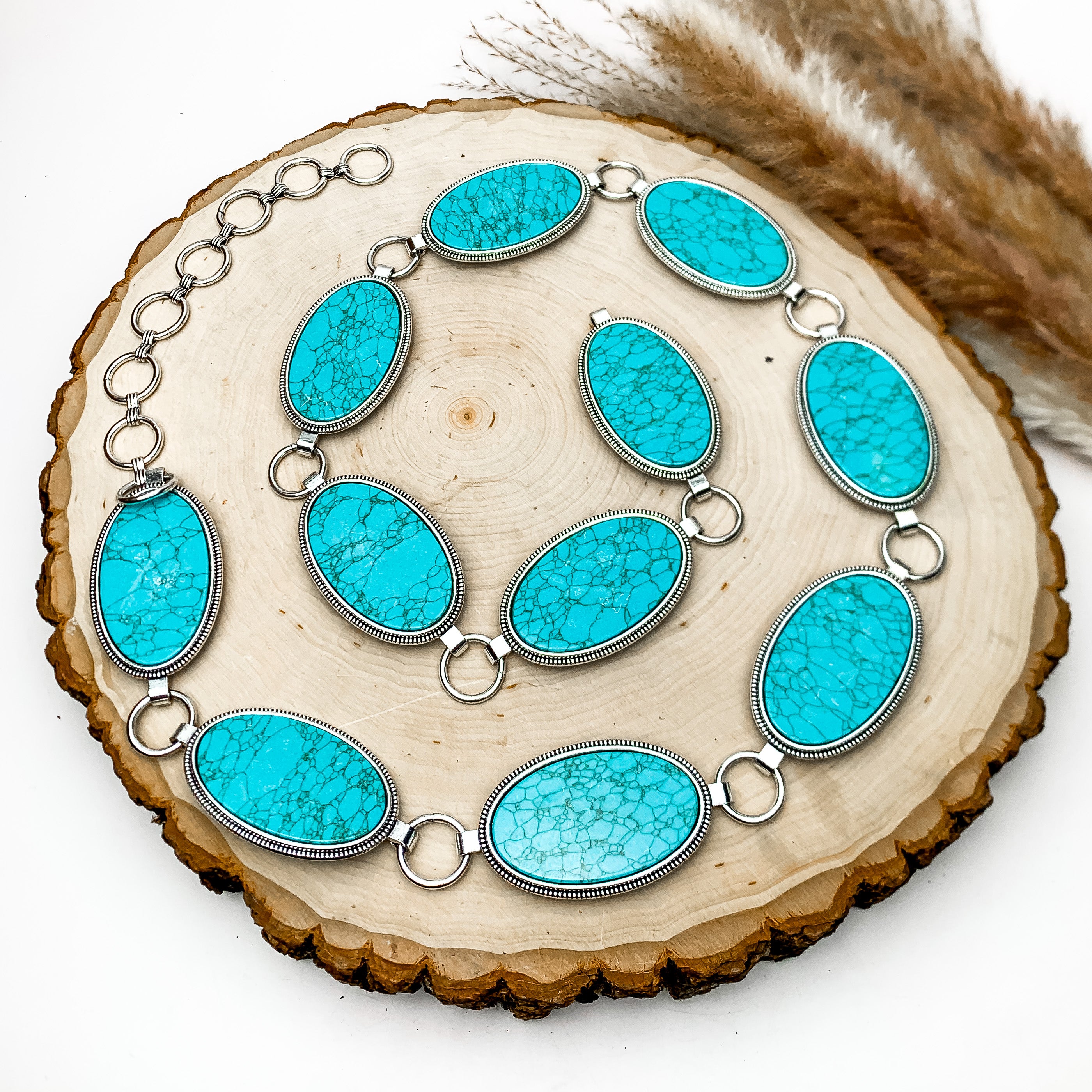 Western Oval Silver Tone adjustable Belt in Turquoise. This belt is laying in a circle formation on a tree stump. The background of the photo is white.