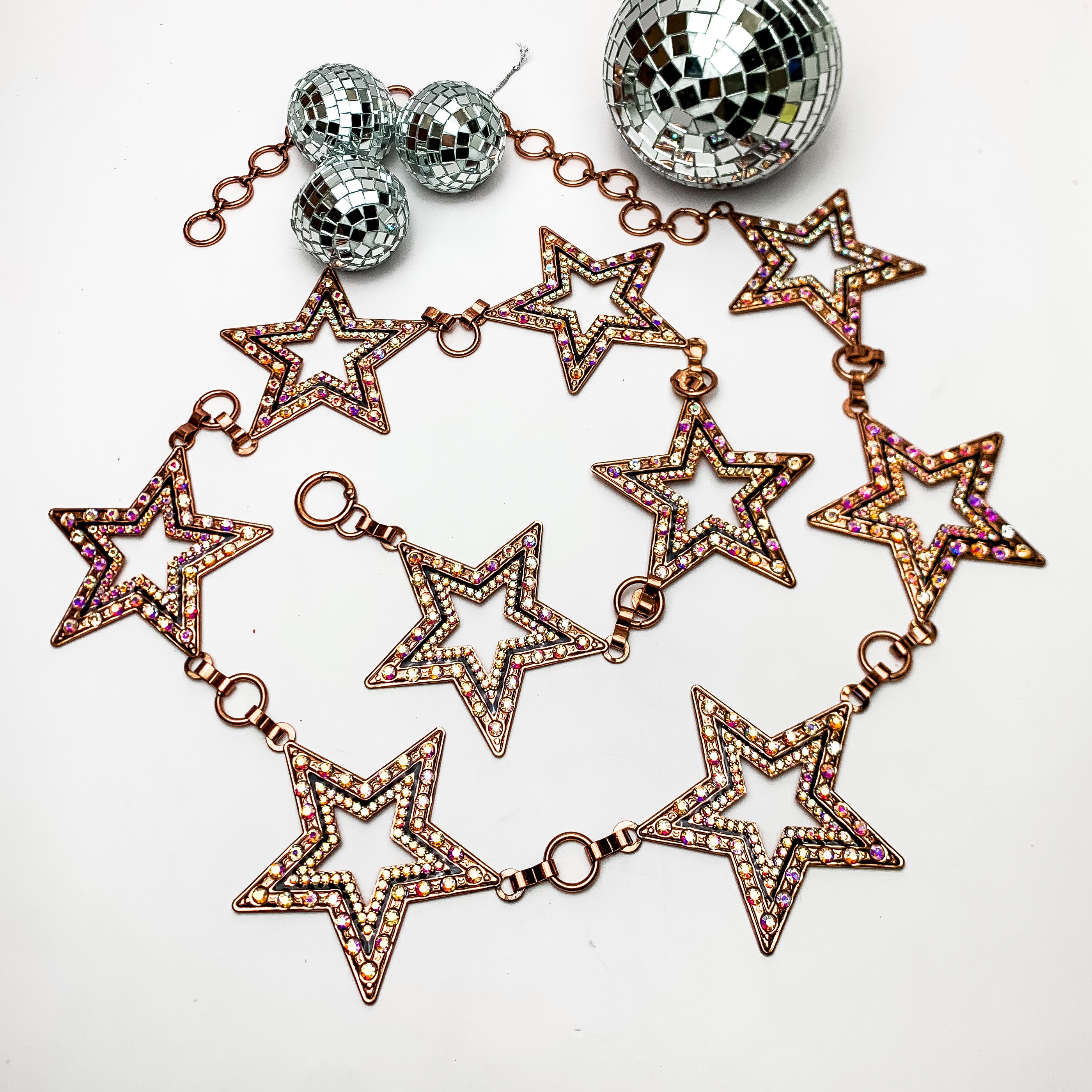 Starlight Adjustable Copper Belt With Ab Crystals. This belt is on a white background with disco balls above them for decoration.
