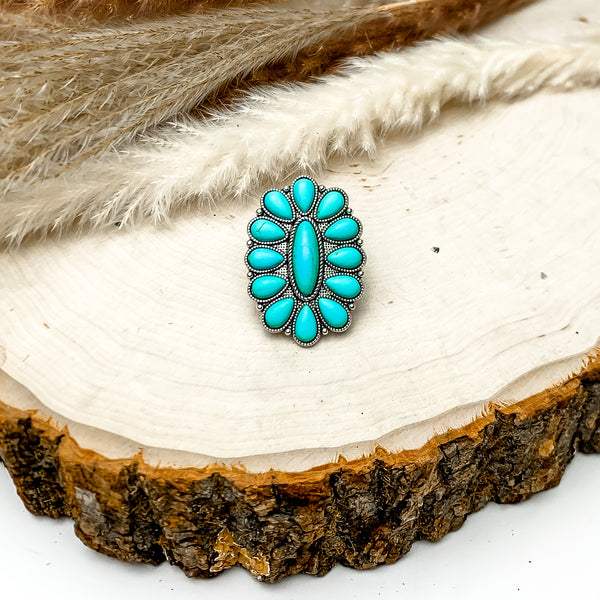 Silver Tone Flower Stone Ring in Turquoise. This cluster stone ring is pictured on a wood piece with feathers behind the ring.