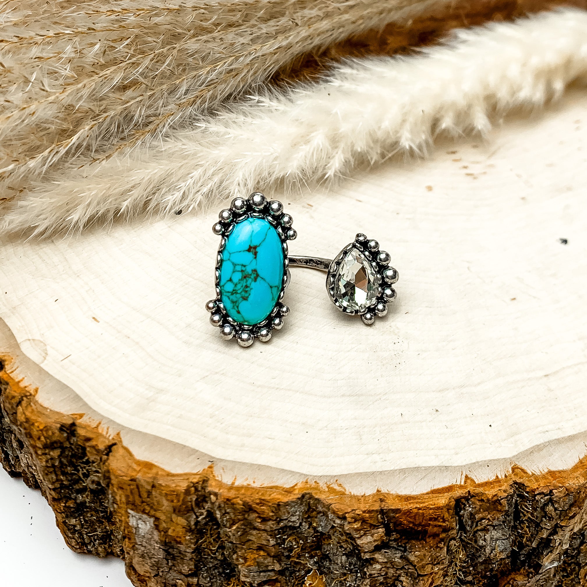 Duo Finger Ring With Turquoise Blue Stone and Clear Crystal. The ring is pictured on a wood piece with feathers behind it.