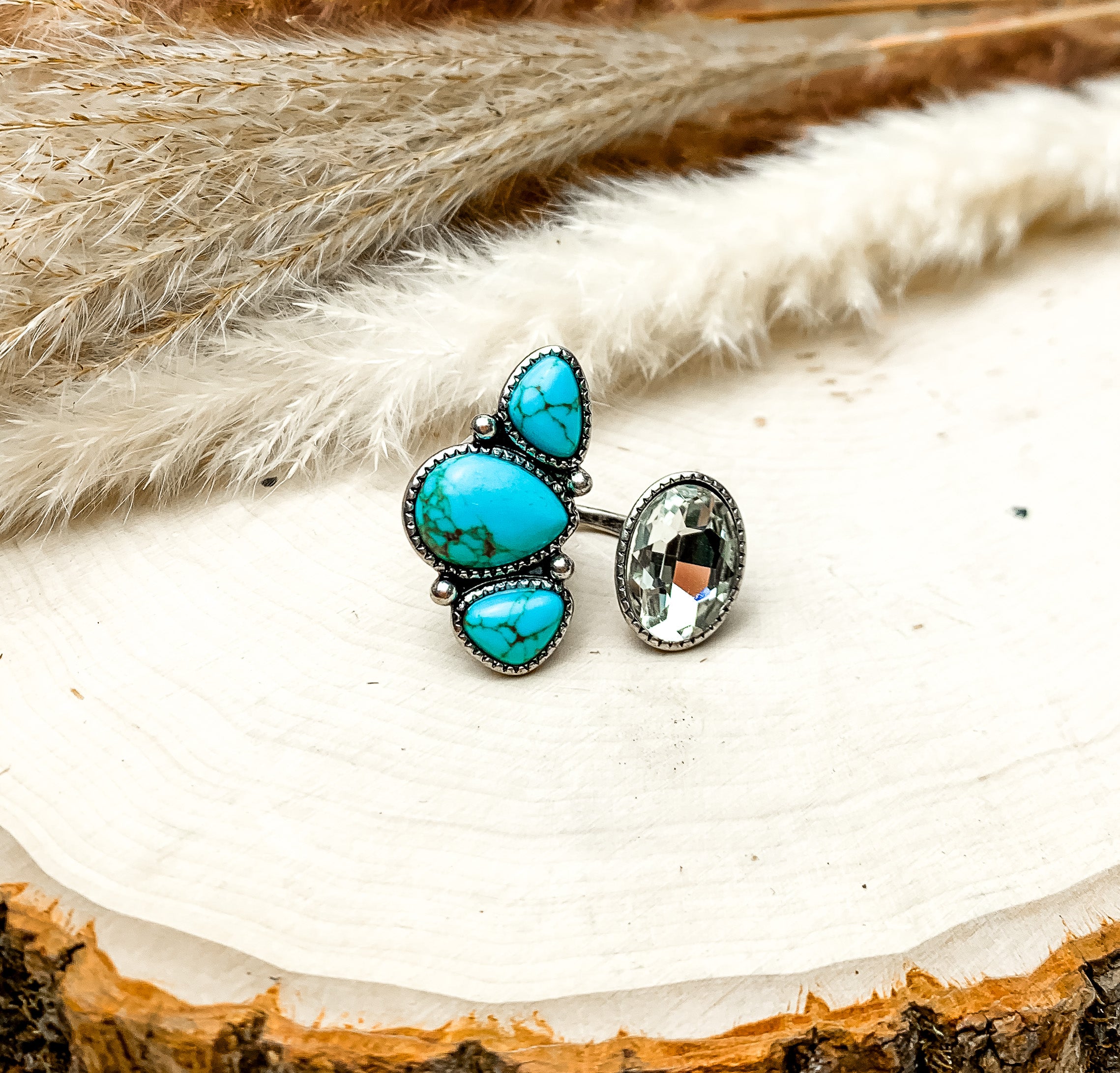 Duo Finger Ring With multiple Turquoise Blue Stones a and Clear Crystal. The ring is pictured on a wood piece with feathers behind it.