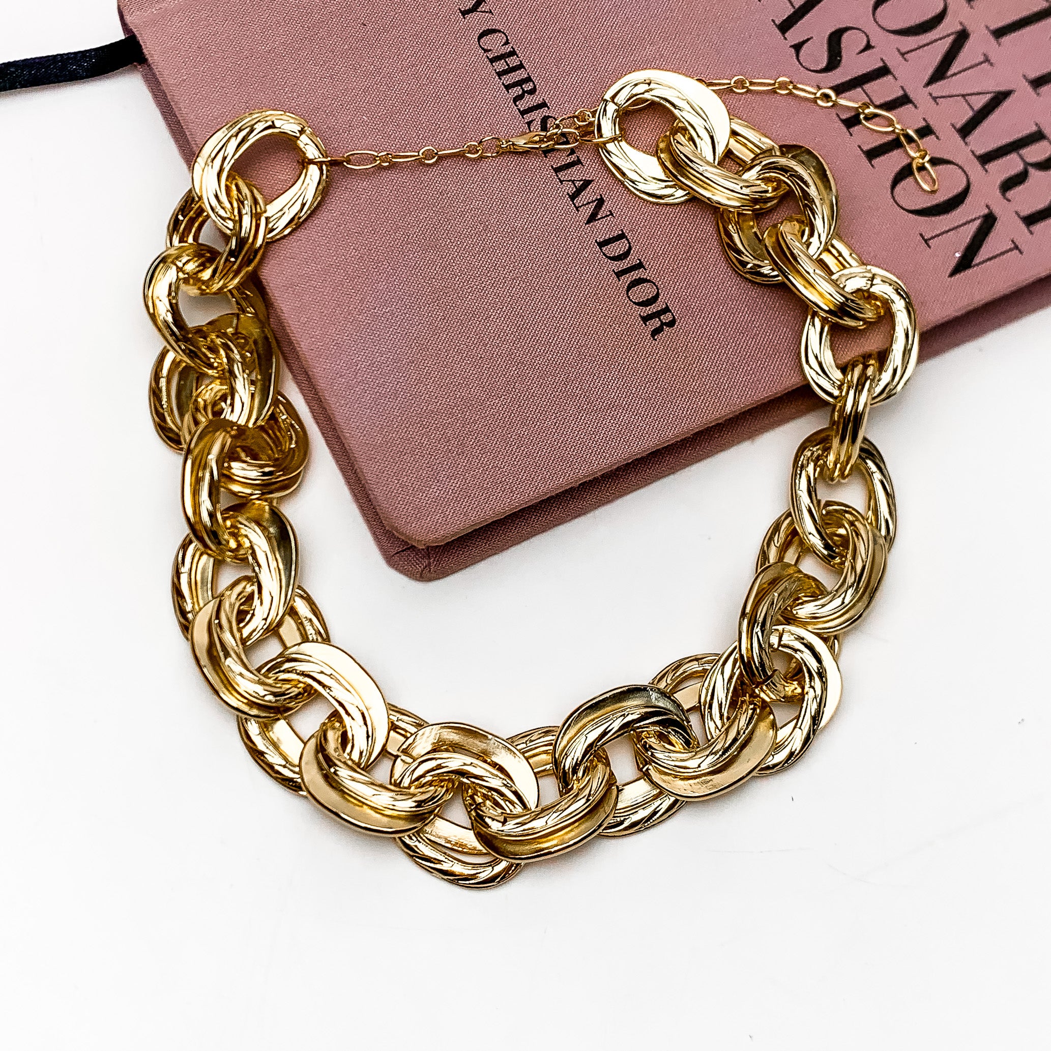 Fall Fashion Gold Tone Chain Necklace. This gold chain necklace is pictured on a white background with a pink book behind it.