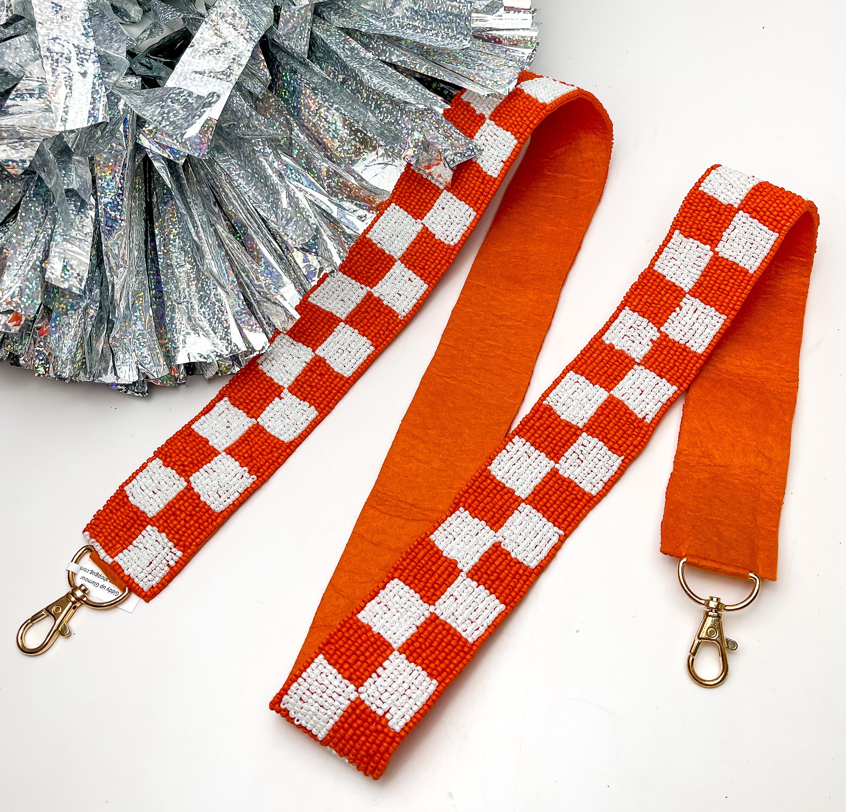 Game Day! Checkered Beaded Purse Strap in Orange and White. This purse strap is pictured on a white background with a silver pom pom next to it.