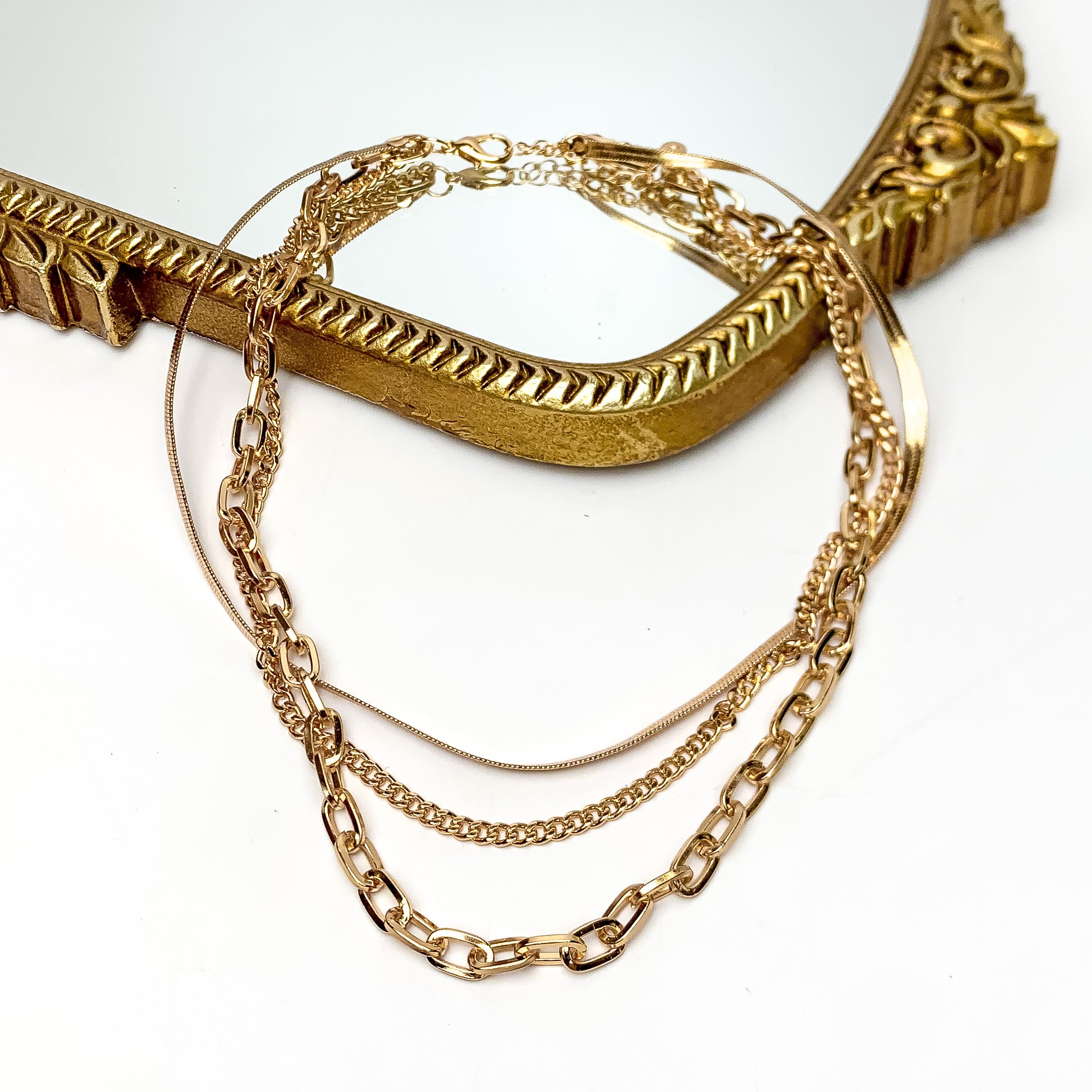 Friday Night Fun Multi Strand Chain Necklace in Gold Tone. This gold tone necklace is on a white background with part of it on a gold trimmed mirror.