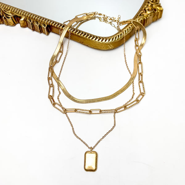 Three Strand Gold Tone Necklace With Rectangle Pendant. This necklace is pictured on a white background with the necklace on a gold mirror.