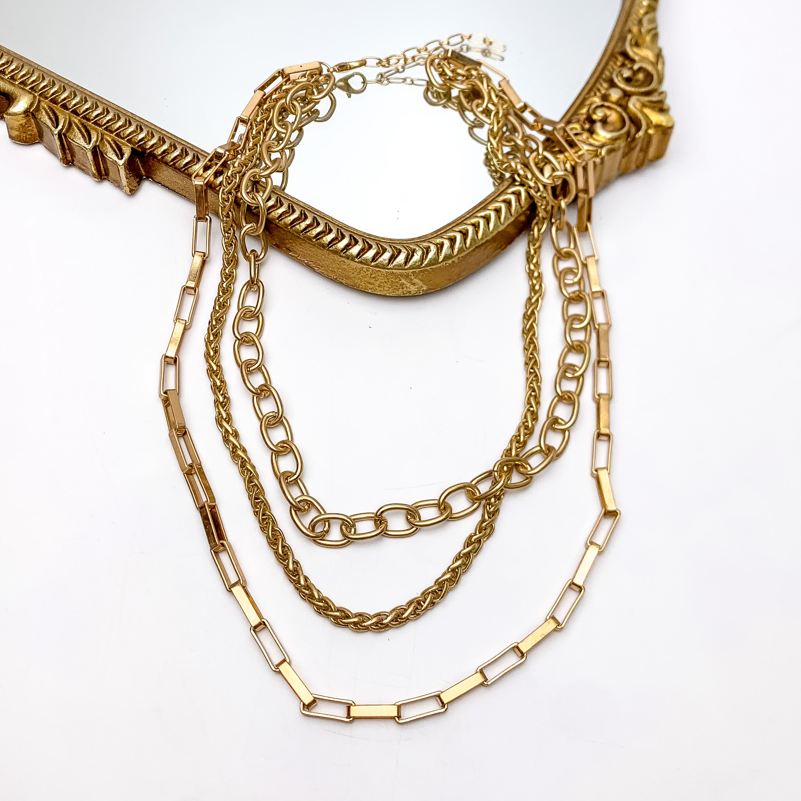 Triple Strand Variety Gold Tone Chain Necklace. This necklace is pictured on a white background with part of it laying on a gold trimmed mirror.