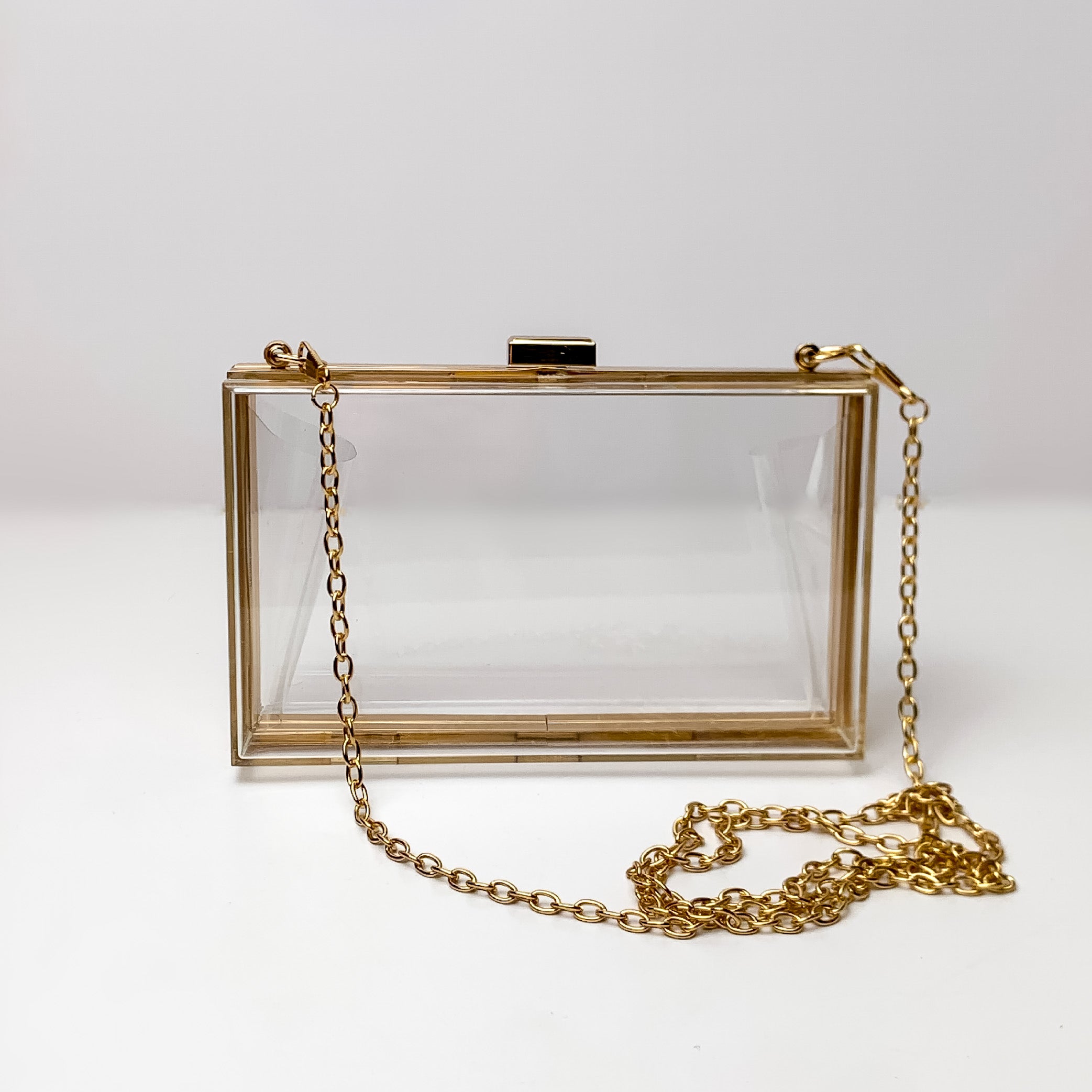 Clear rectangle purse with a gold outline and gold chain strap pictured on a white background. 