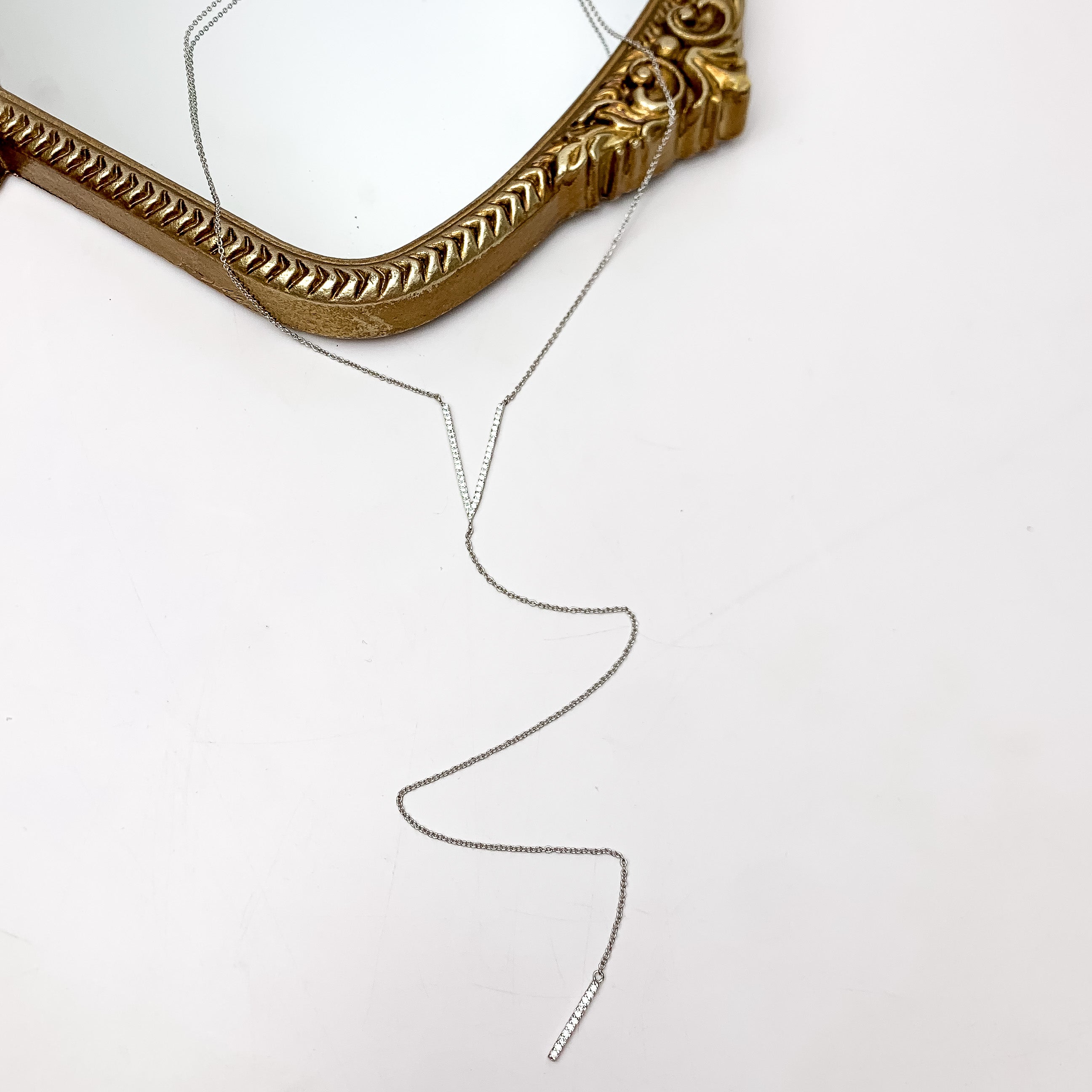 Here For It Silver Tone Y Necklace With Clear Crystals. This necklace is pictured on a white background with part of it on a gold trimmed mirror.
