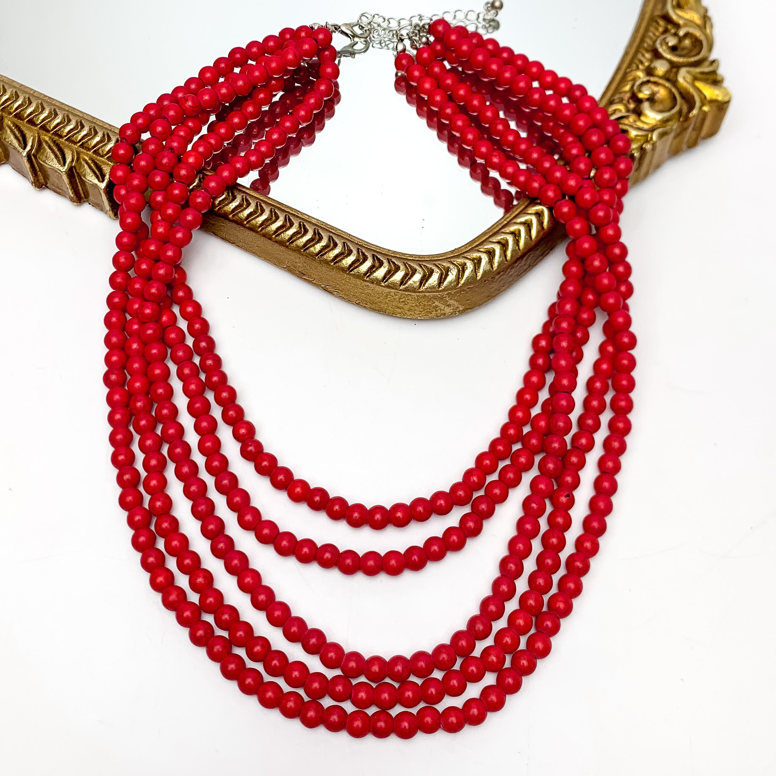  Five Strand Red Beaded Necklace. This necklace is pictured on a white background with part of it on a gold trimmed mirror.