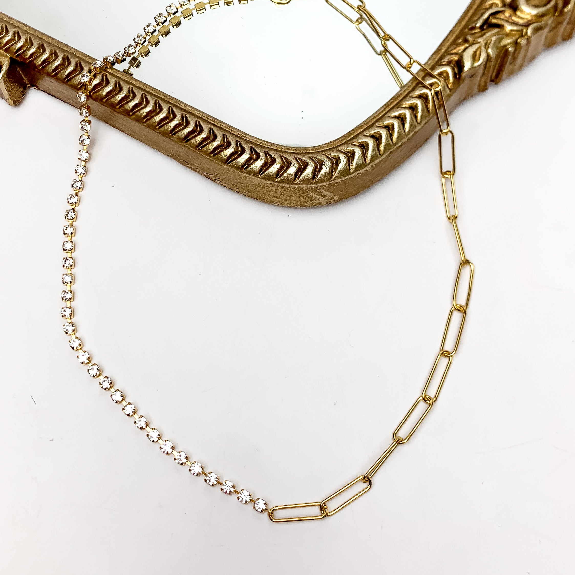 Drama Queen Gold Tone Necklace With Clear Crystals. This necklace is pictured on a white background with part of it on a gold trimmed mirror.