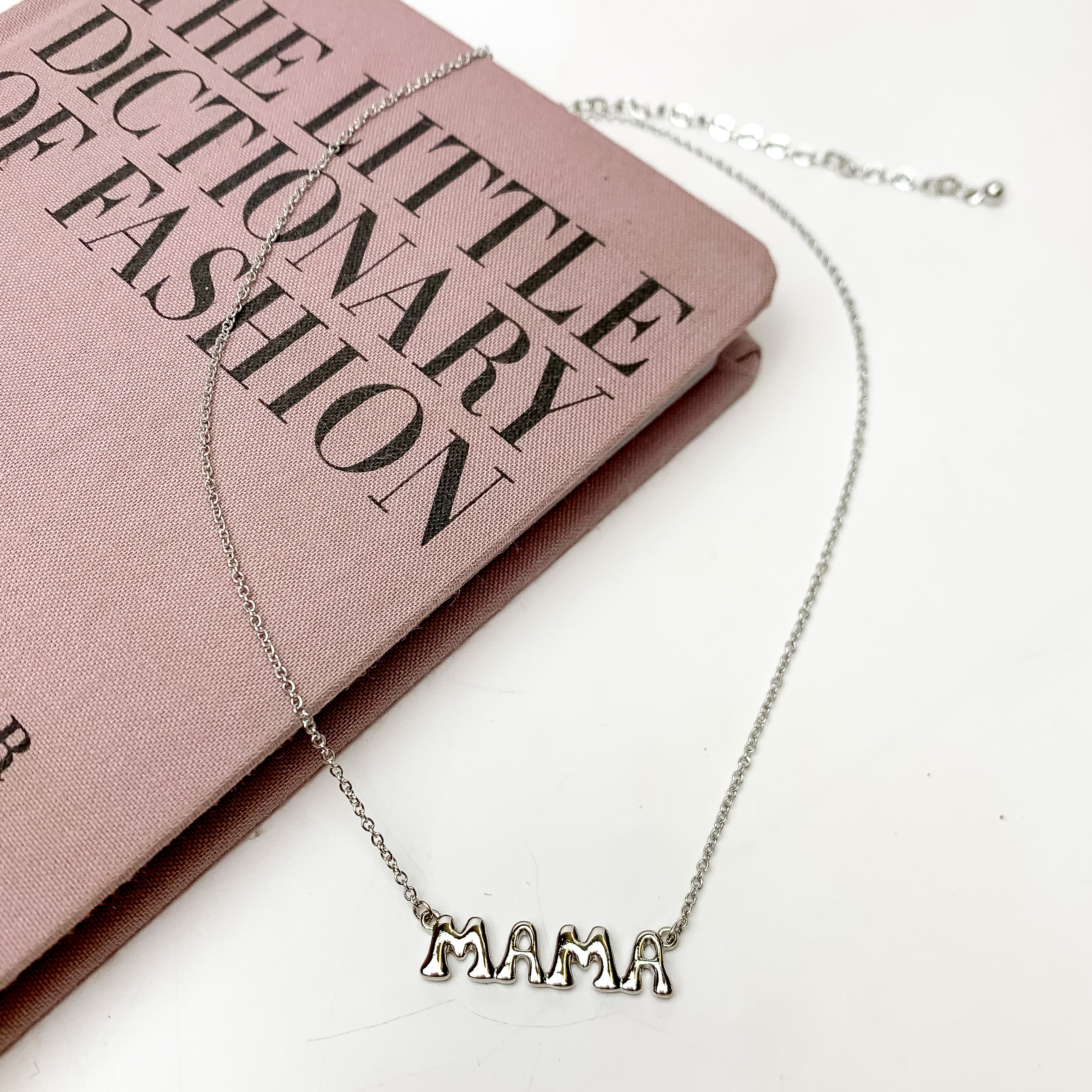 Mama Bubble Letter Chain Necklace in Silver Tone. This necklace is pictured on a white background with part of it on a pink book.