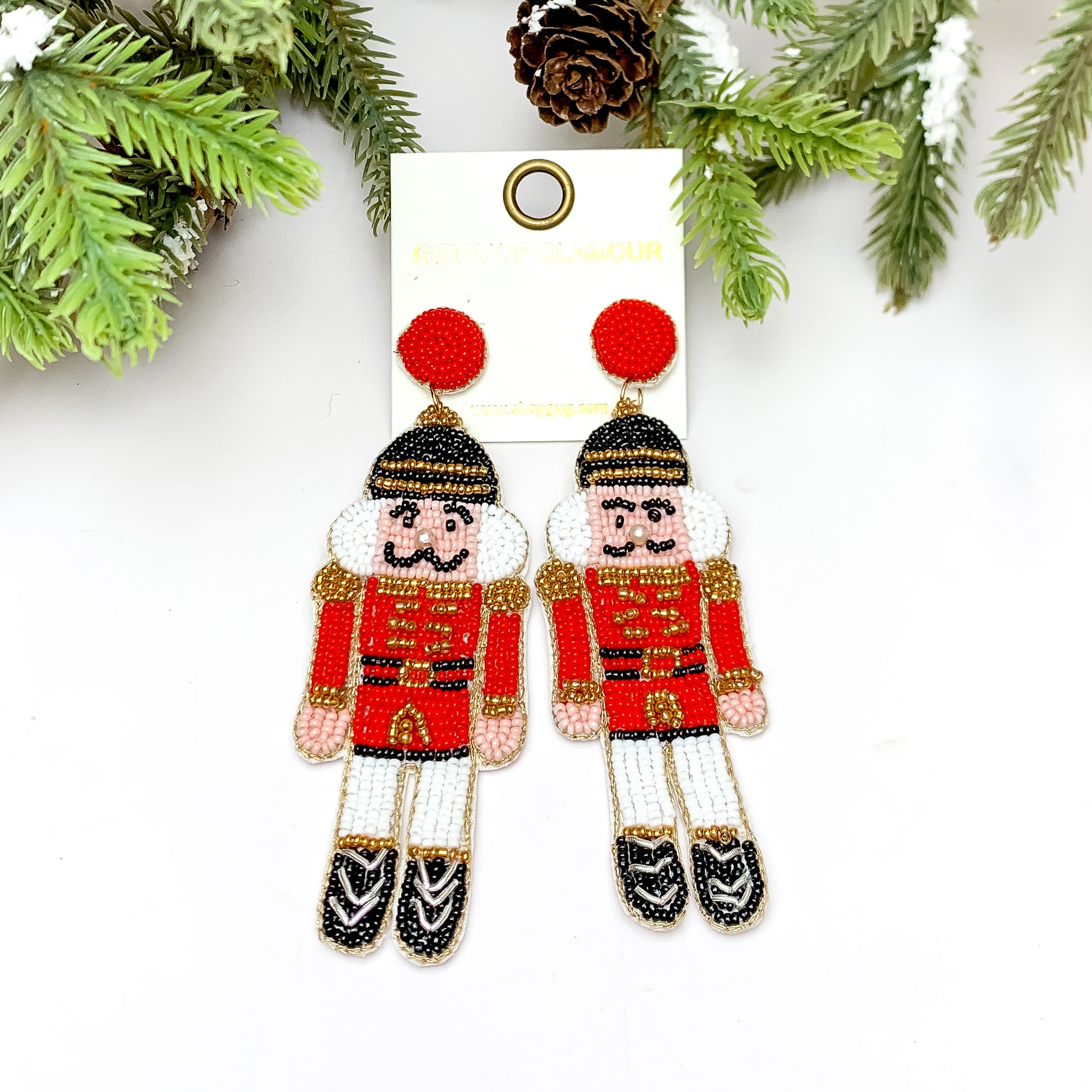Nutcracker Beaded Earrings in Red. These earrings are pictured on a white background with a tree and pine cones at the top.