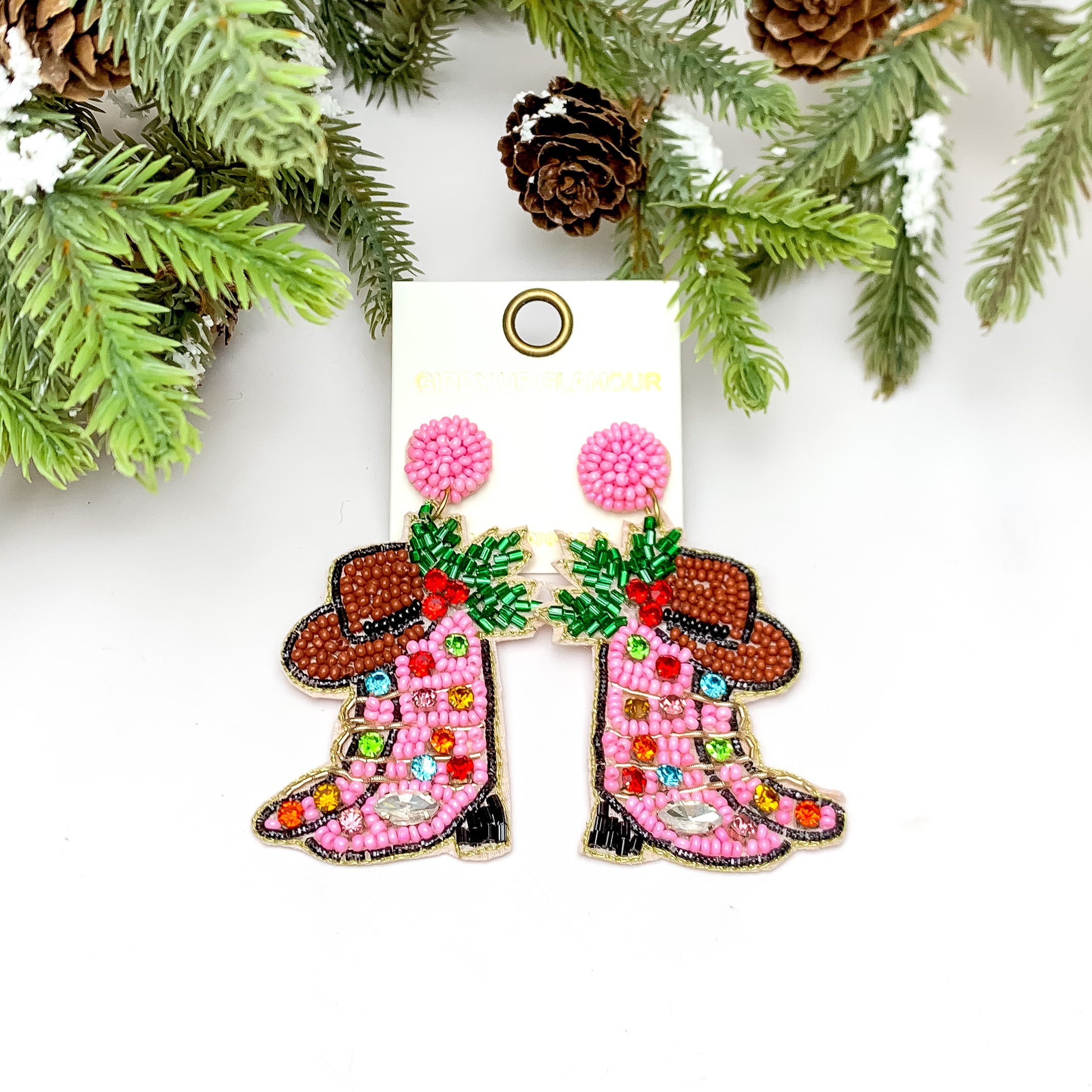 Cowgirl Christmas Beaded Boot Earrings in Pink. These earrings are pictured on a white background with a tree and pine cones at the top.