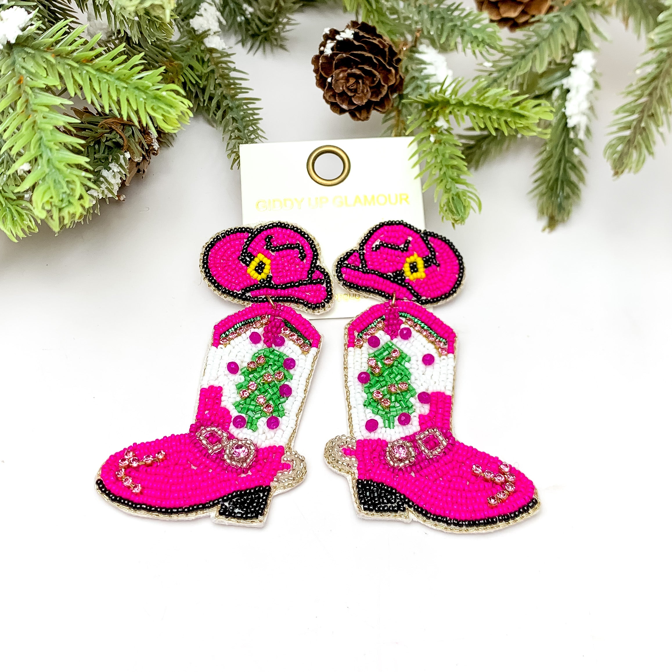 Cowgirl Christmas Beaded Boot Earrings With Hat Post in Pink. These earrings are pictured on a white background with a tree and pine cones at the top.