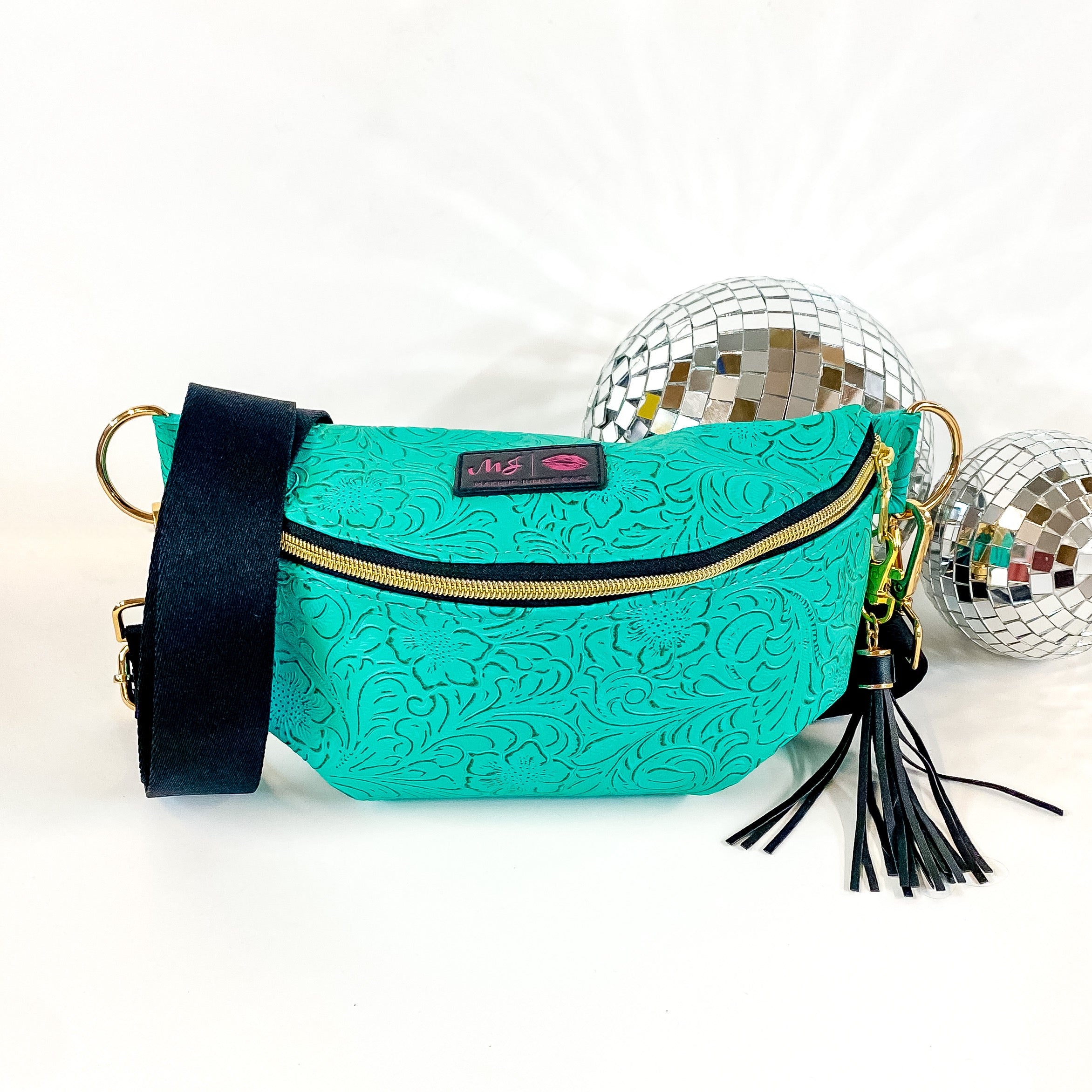 Pictured on a white background with disco balls in the background is a sidekick bag in a turquoise leather tooled print. This bag includes a middle zipper and a tassel.