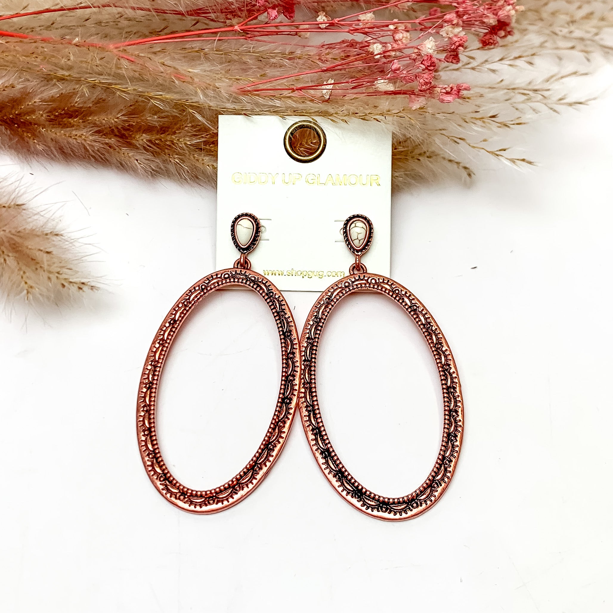Oval Large Copper Tone Earrings With Ivory Posts. These earrings are pictured on a white background with plants behind for decoration.