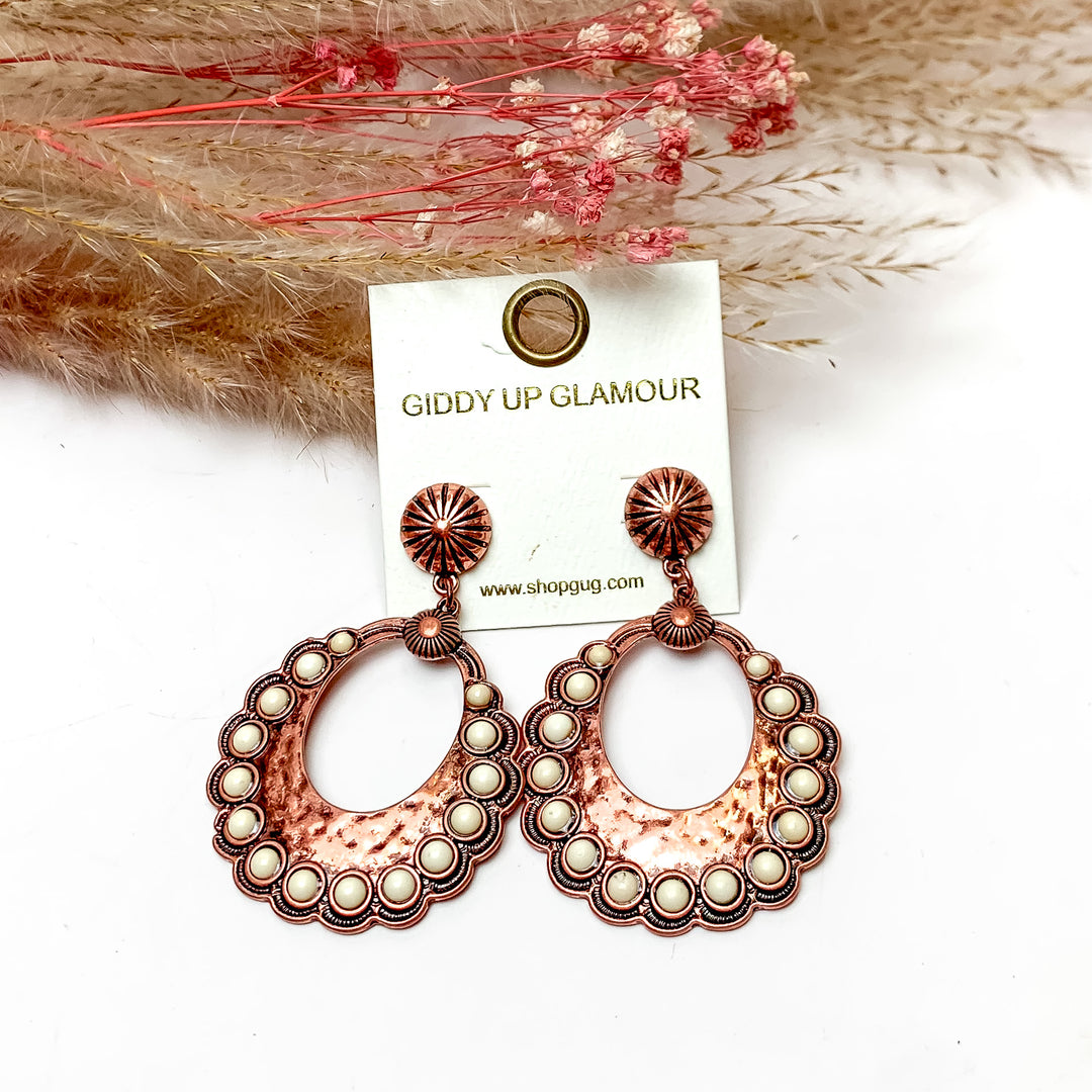Western Open Copper Tone Earrings With Ivory Stones. These earrings are pictured on a white background with plants behind for decoration.