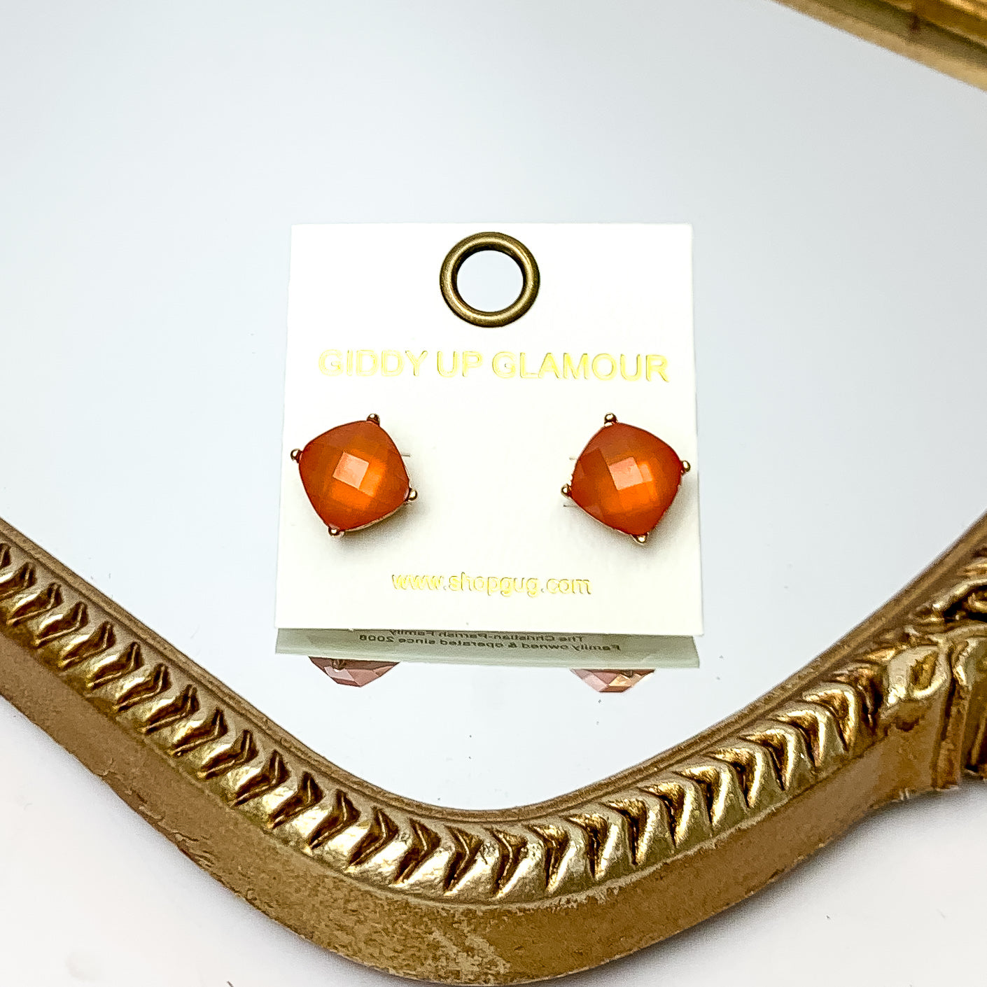 Large Crystal Stud Earrings in Orange. These earrings are pictured laying on a gold trimmed mirror.