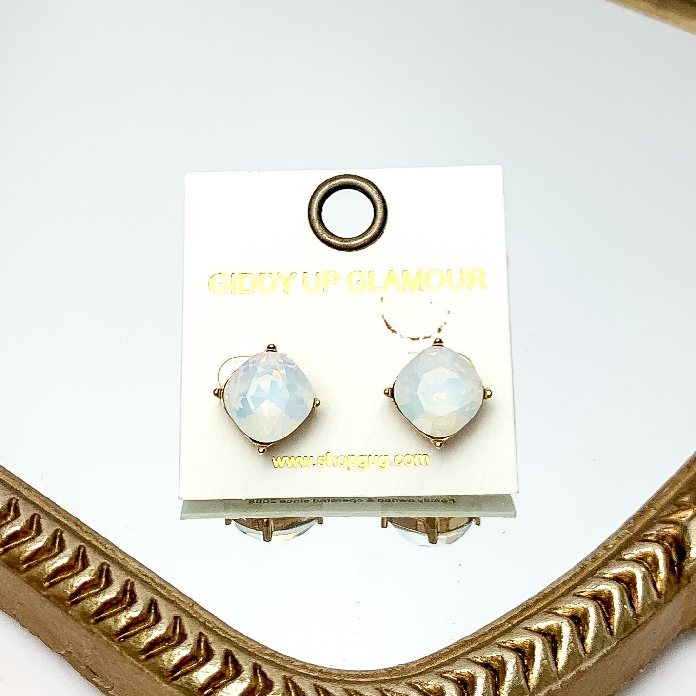 Large Crystal Stud Earrings in White Opal. These earrings are pictured laying on a gold trimmed mirror.