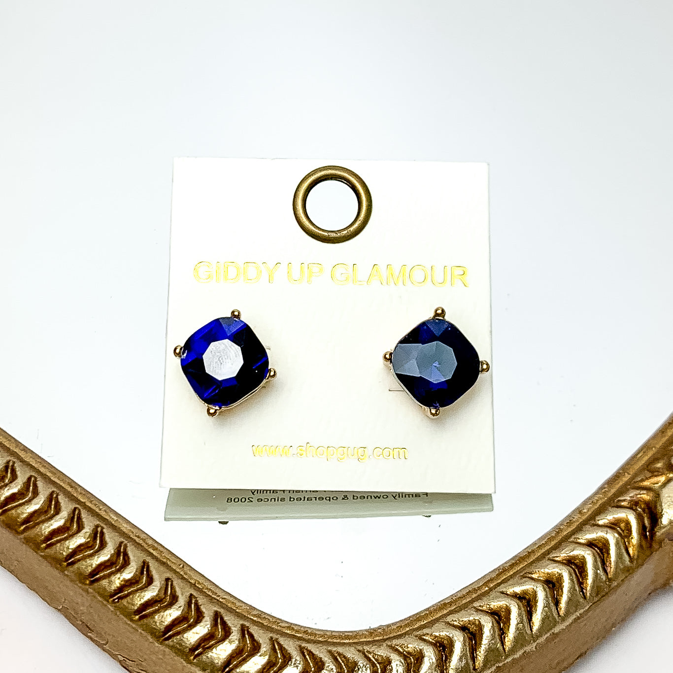 Large Crystal Stud Earrings in Navy Blue. These earrings are pictured laying on a gold trimmed mirror. 