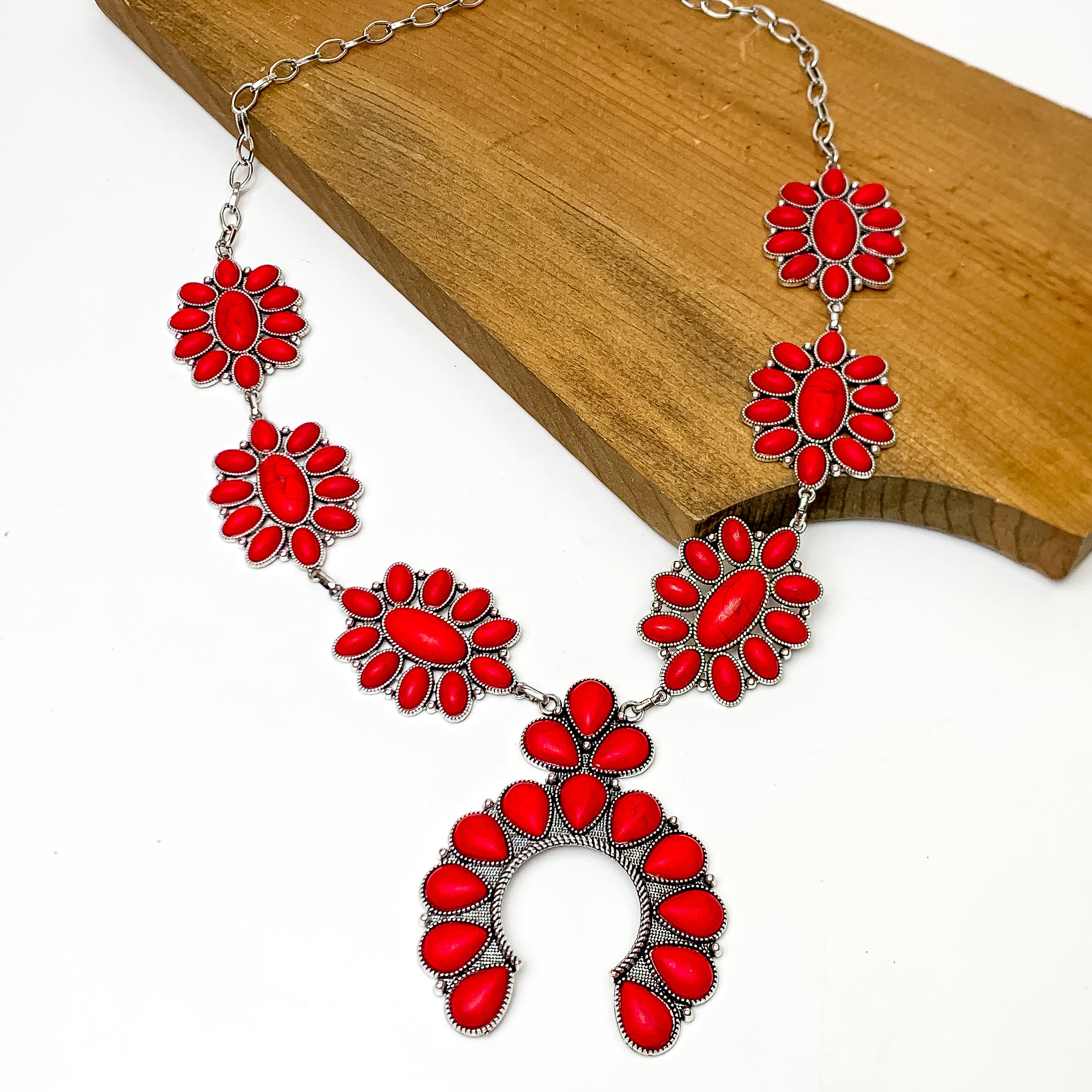 Squash Necklace with Oval Flowers in Silver Tone and Red. This necklace is pictured on a white background laying against a wood piece.
