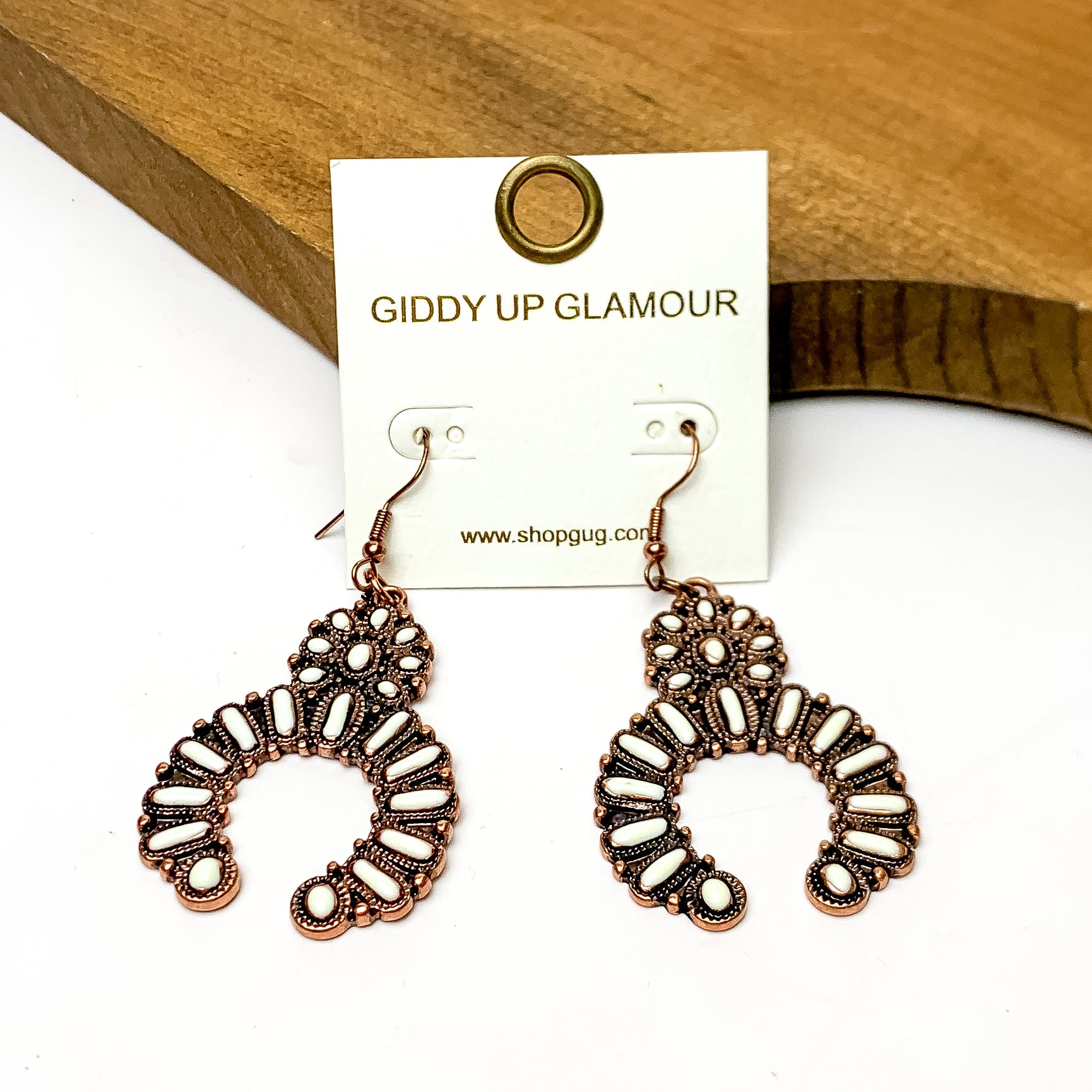 Squash Blossom Copper Tone Medium Earrings in Ivory. These earrings are pictured on a white background and are laying against a wood piece.