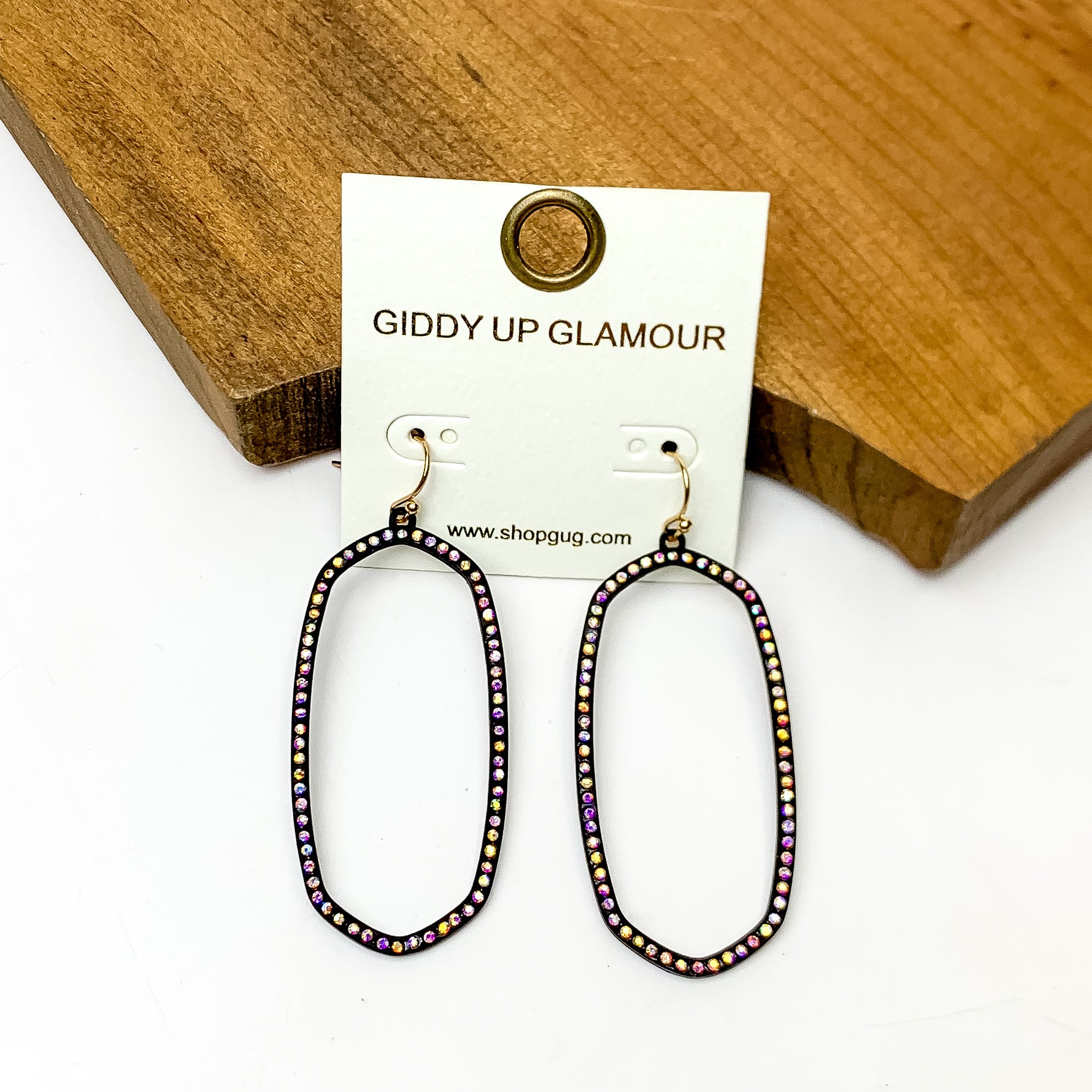 Sparkle Girl Open Oval Earrings in Black. These earrings are pictured laying against a wood piece with a white background.