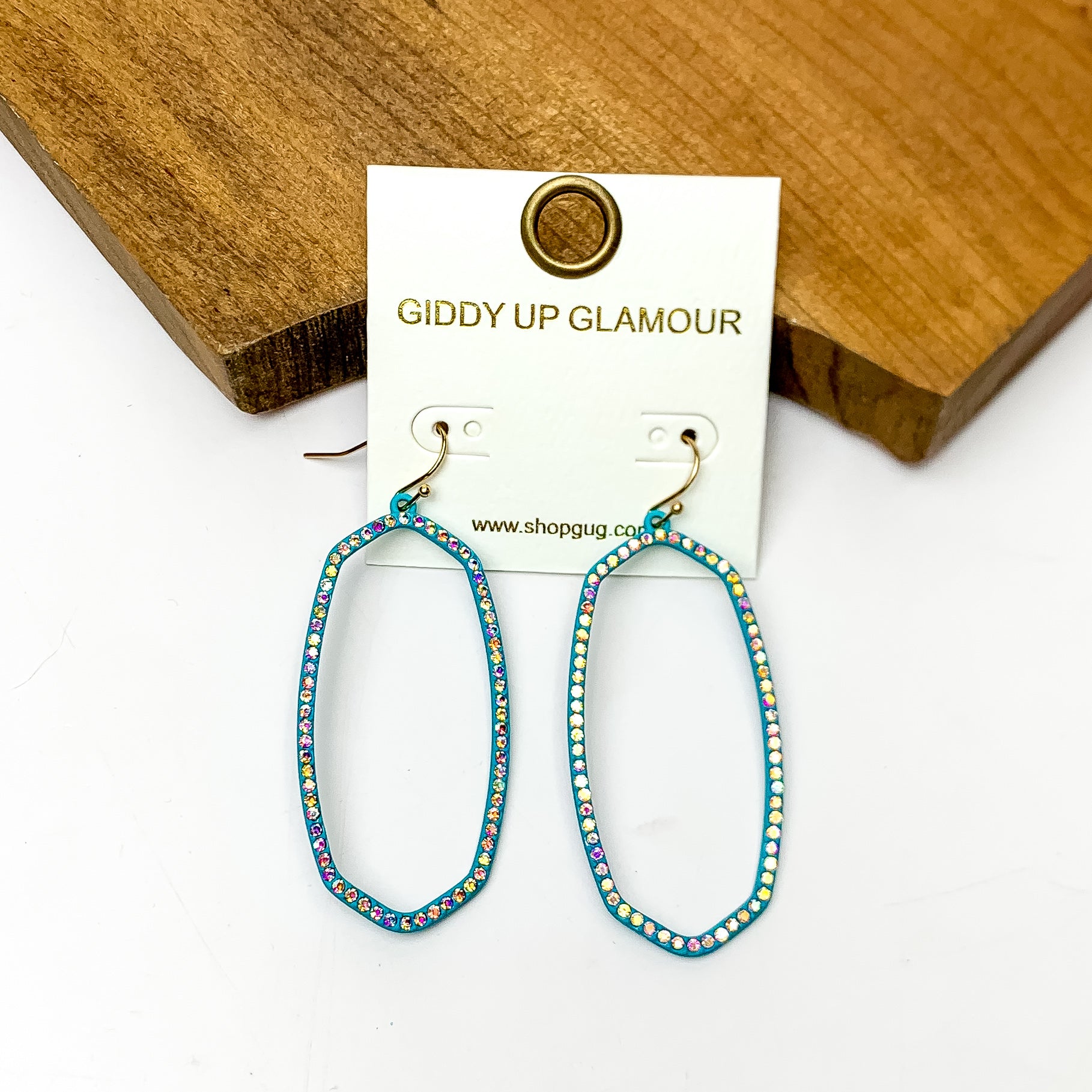 Sparkle Girl Open Oval Earrings in Turquoise Blue. These earrings are pictured laying against a wood piece with a white background.