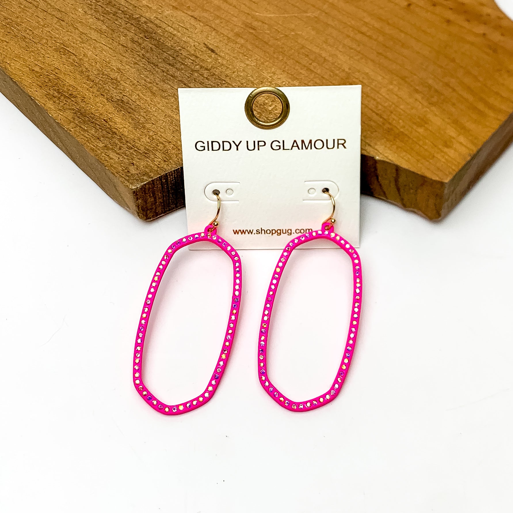 Sparkle Girl Open Oval Earrings in Hot Pink. These earrings are pictured laying against a wood piece with a white background.