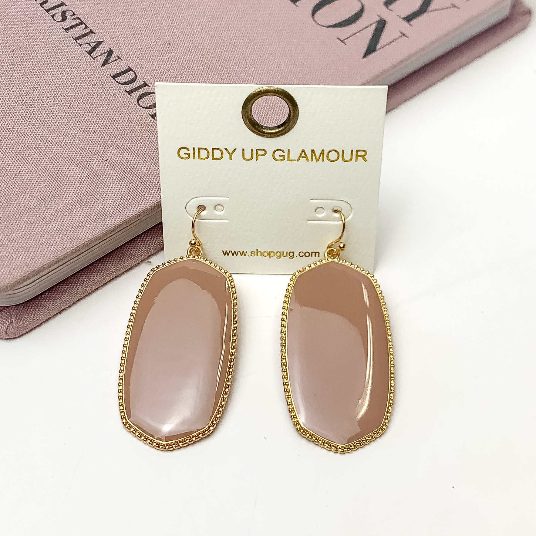 Southern Charm Oval Earrings in Mauve Pink. These earrings are laying on a pink book with a white background behind the book.