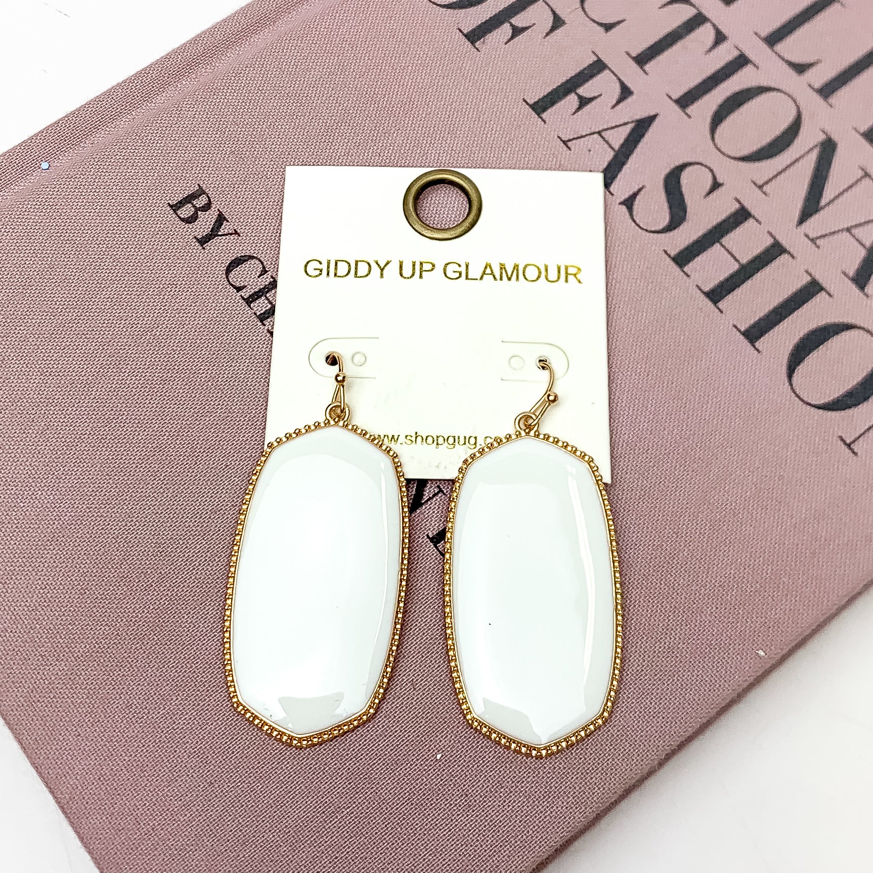 Southern Charm Oval Earrings in White. These earrings are laying on a pink book with a white background behind the book.