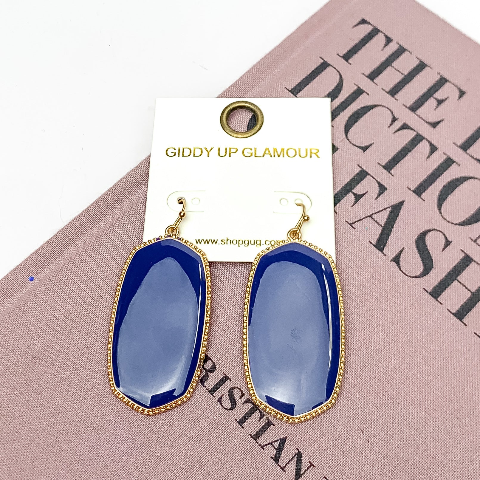Southern Charm Oval Earrings in Navy Blue. These earrings are laying on a pink book with a white background behind the book.