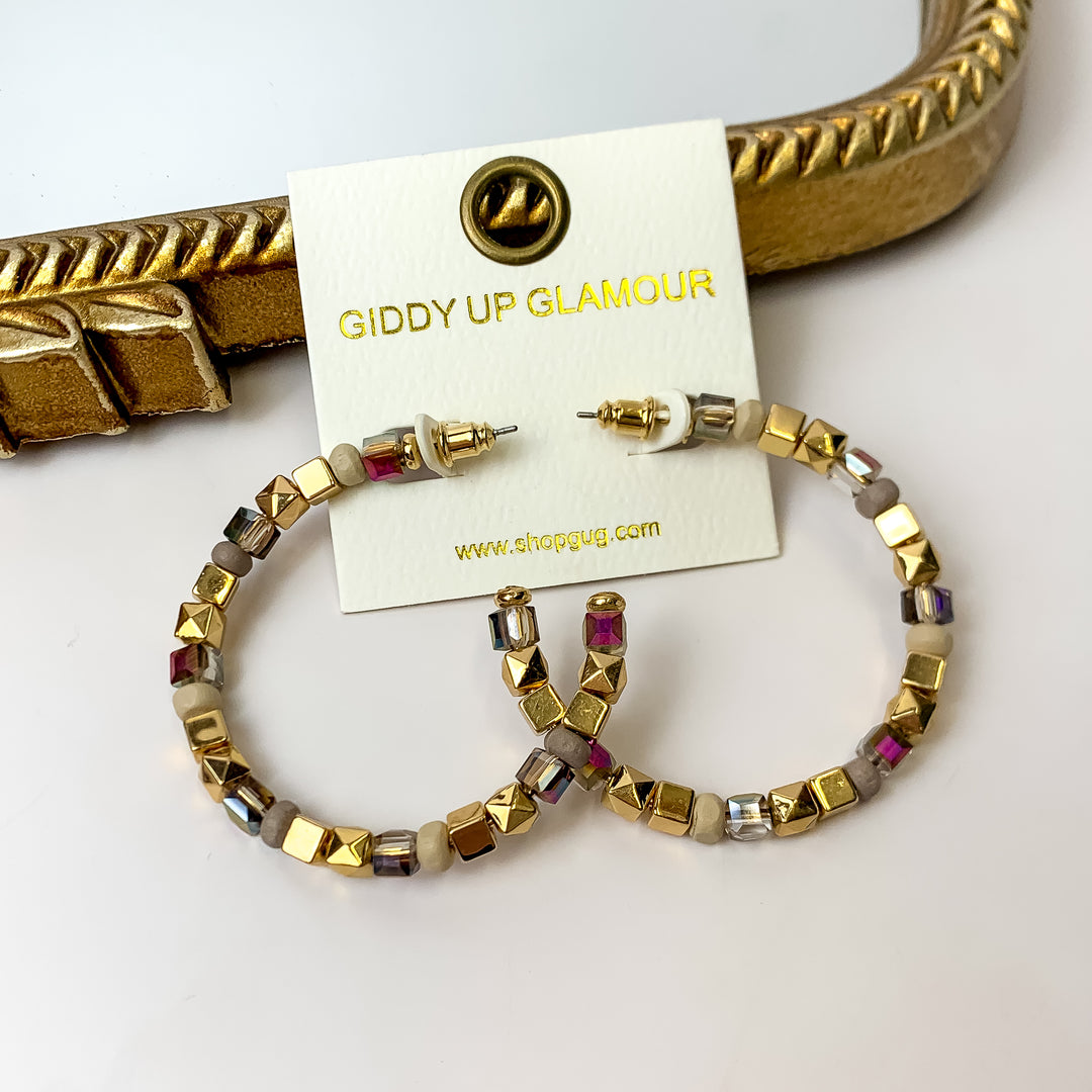 A pair of iridescent neutral beaded hoop earrings on an ivory earring card. These earrings are pictured on a white background with a gold mirror.