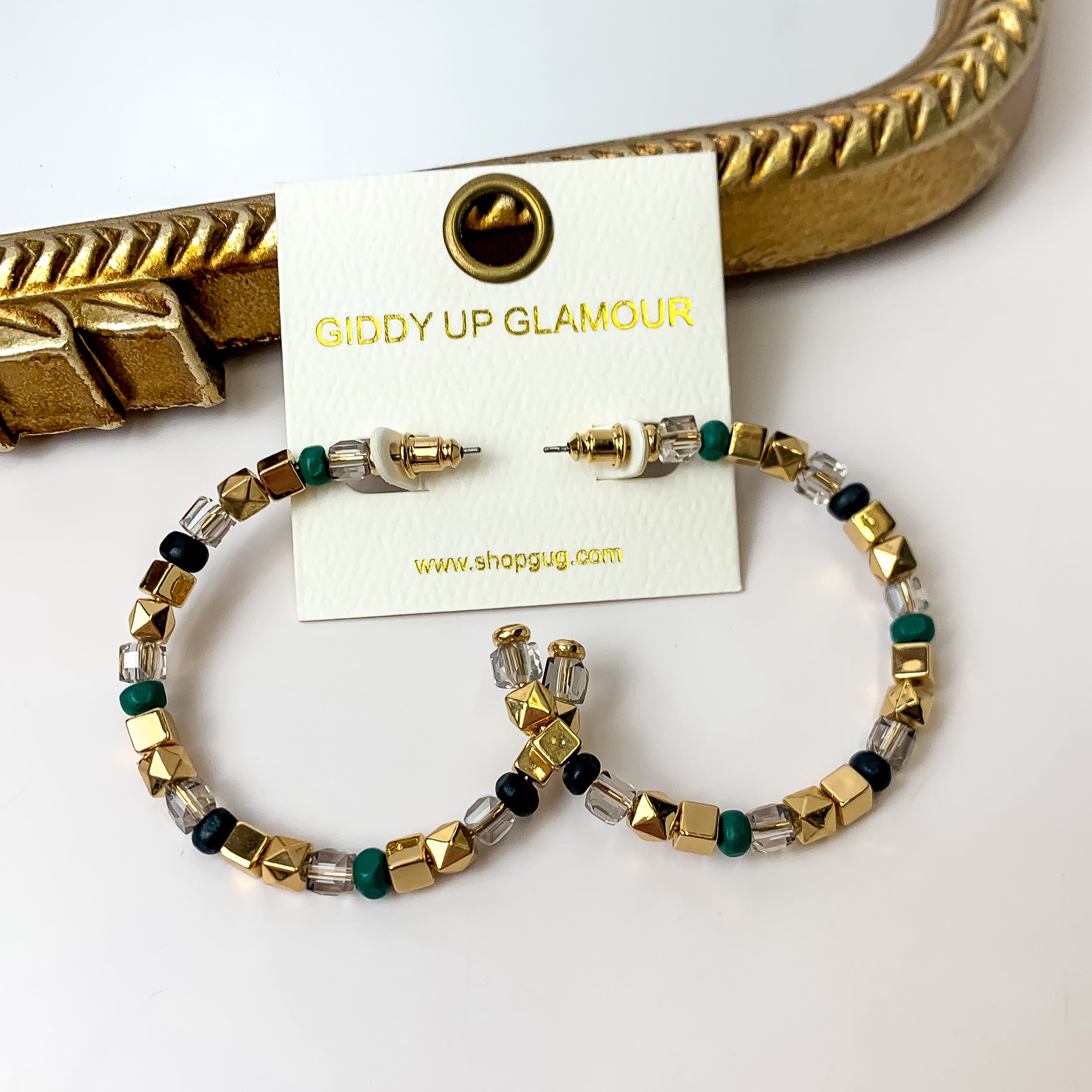 A pair of black, gold, and forest green beaded hoop earrings on an ivory earring card. These earrings are pictured on a white background with a gold mirror.