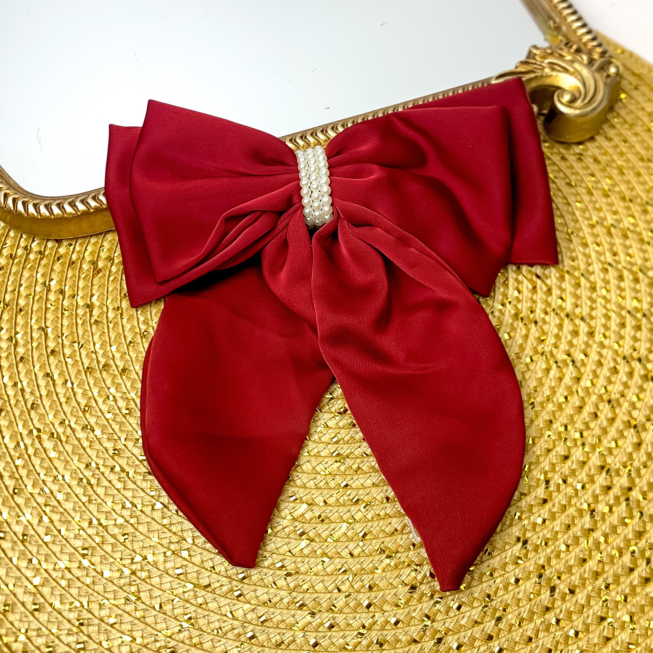 This layered burgundy bow with a pearl canter is laid against a gold mirror and has a gold background.
