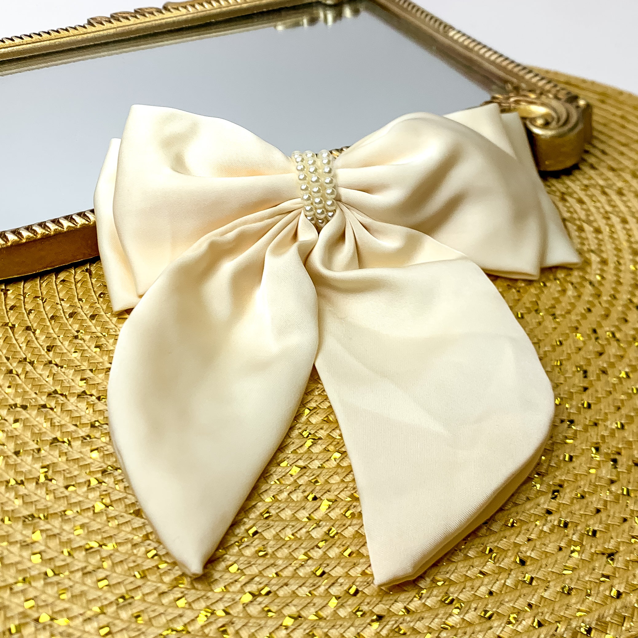 This layered ivory bow with a pearl canter is laid against a gold mirror and has a gold background.