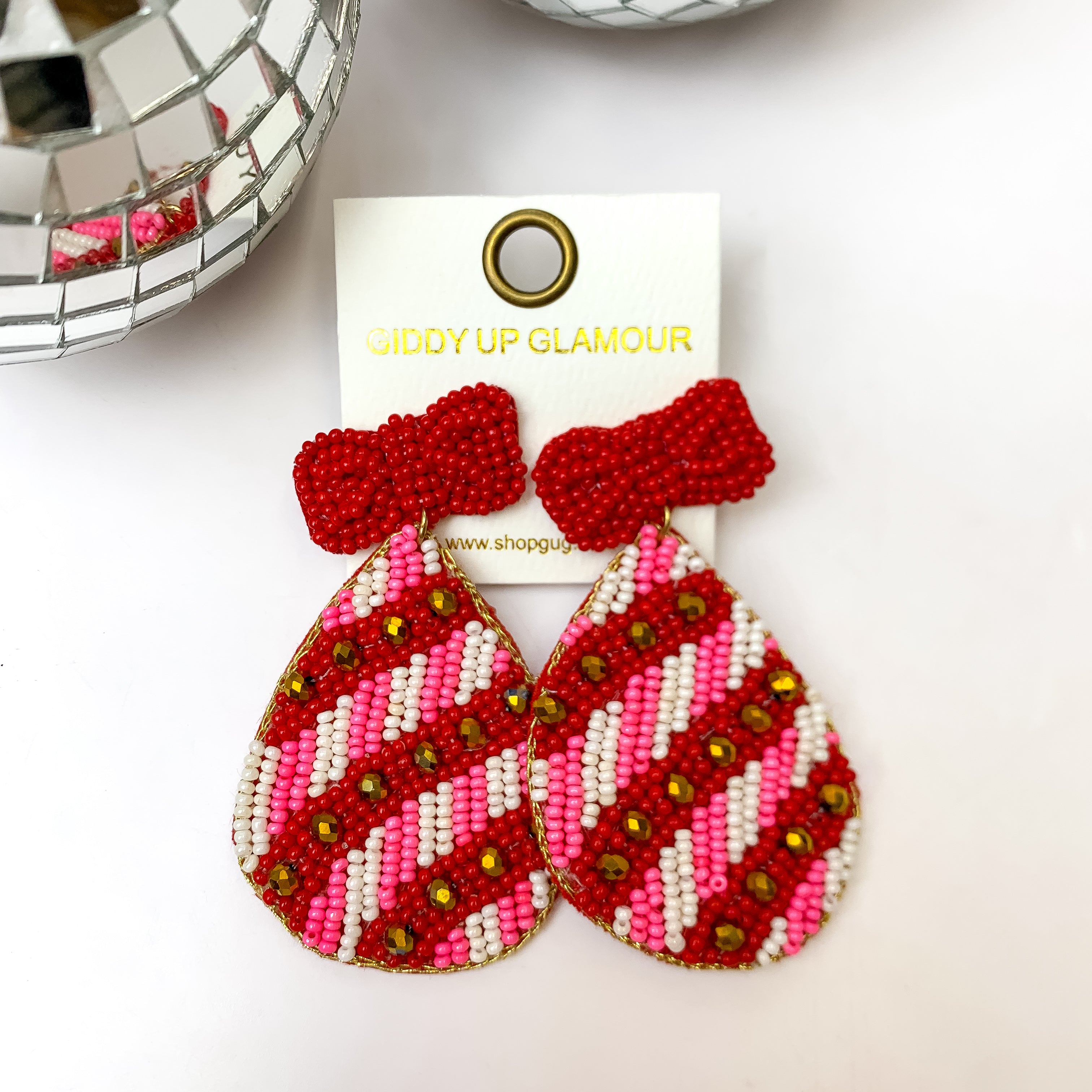 This pair of holiday multi-colored earrings are on an ivory earring card. These earrings are placed on a white background featuring disco balls!