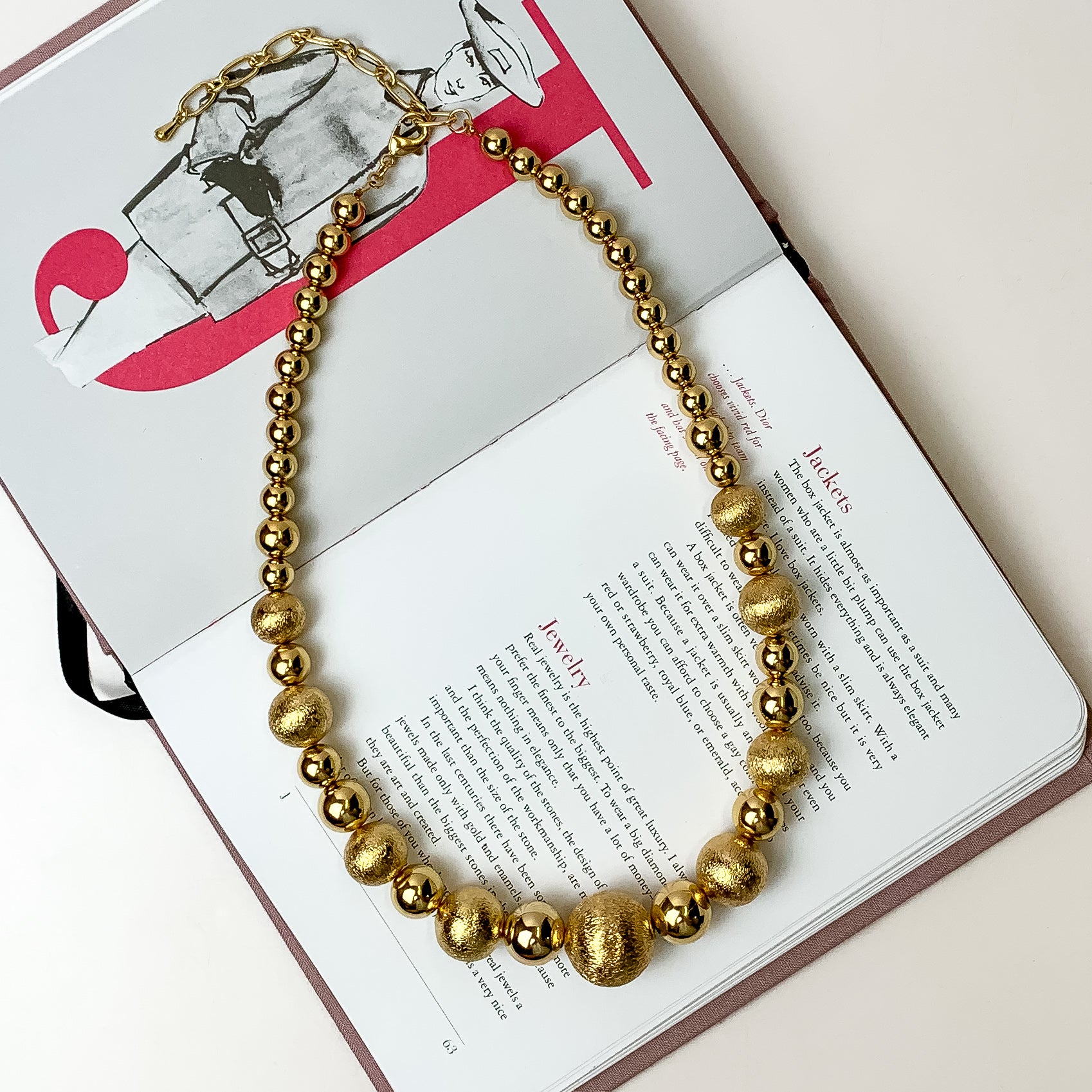 This beaded necklace with gold tone beads is placed inside the pages of a book with a white background.