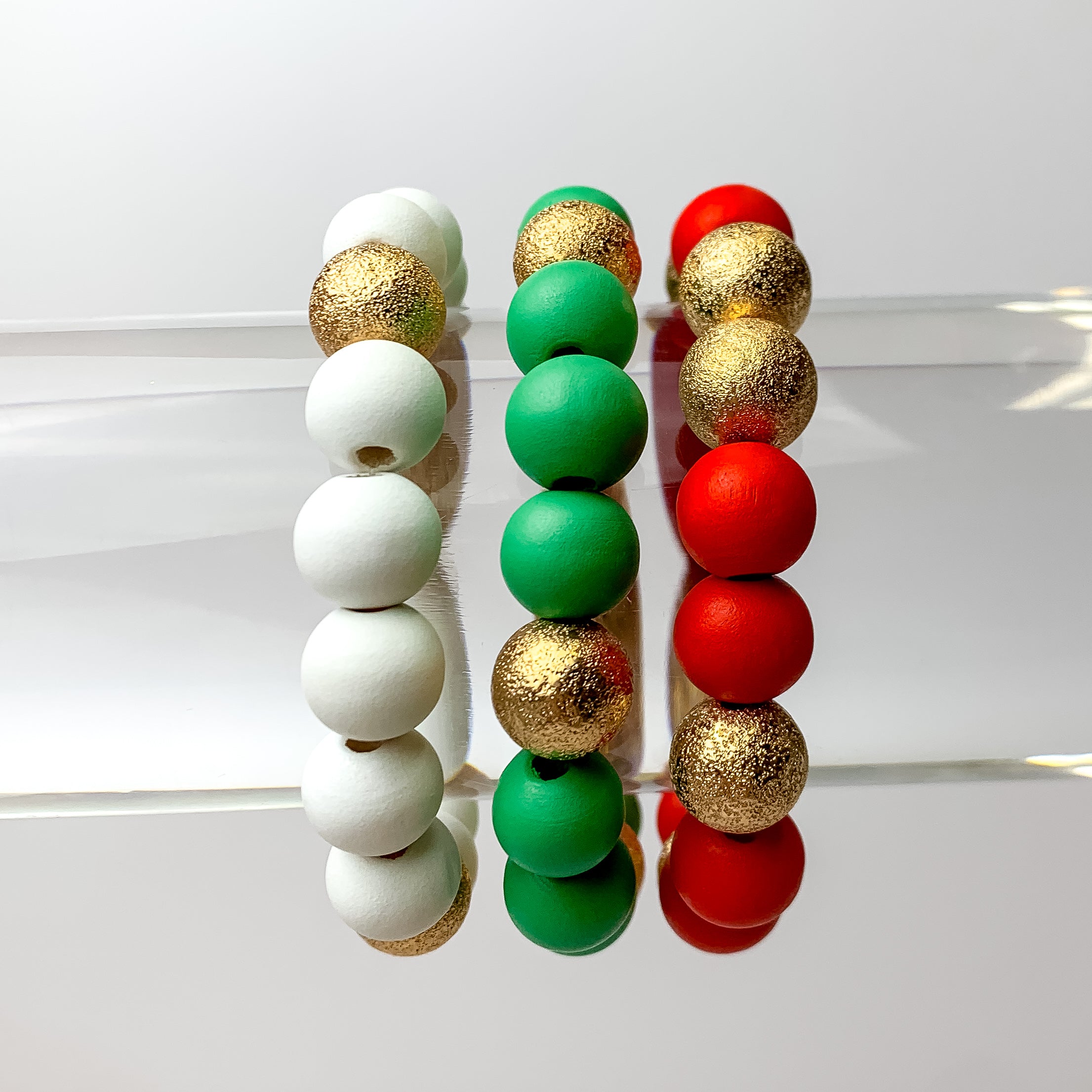 This set of 3 bracelets in the colors red, green, and white are placed on a bracelet display featuring a white background.