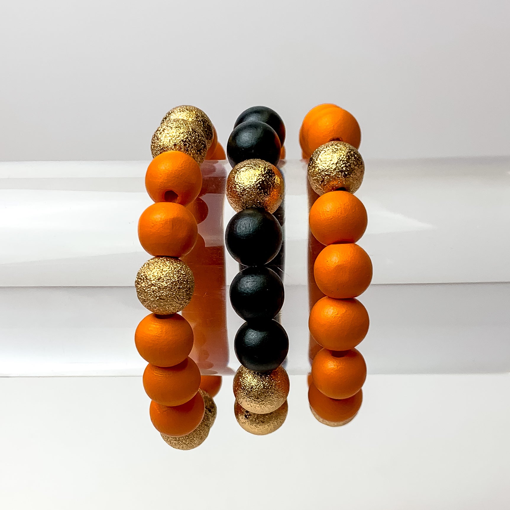 This set of 3 bracelets in the colors orange and black are placed on a clear bracelet display featuring a white background.