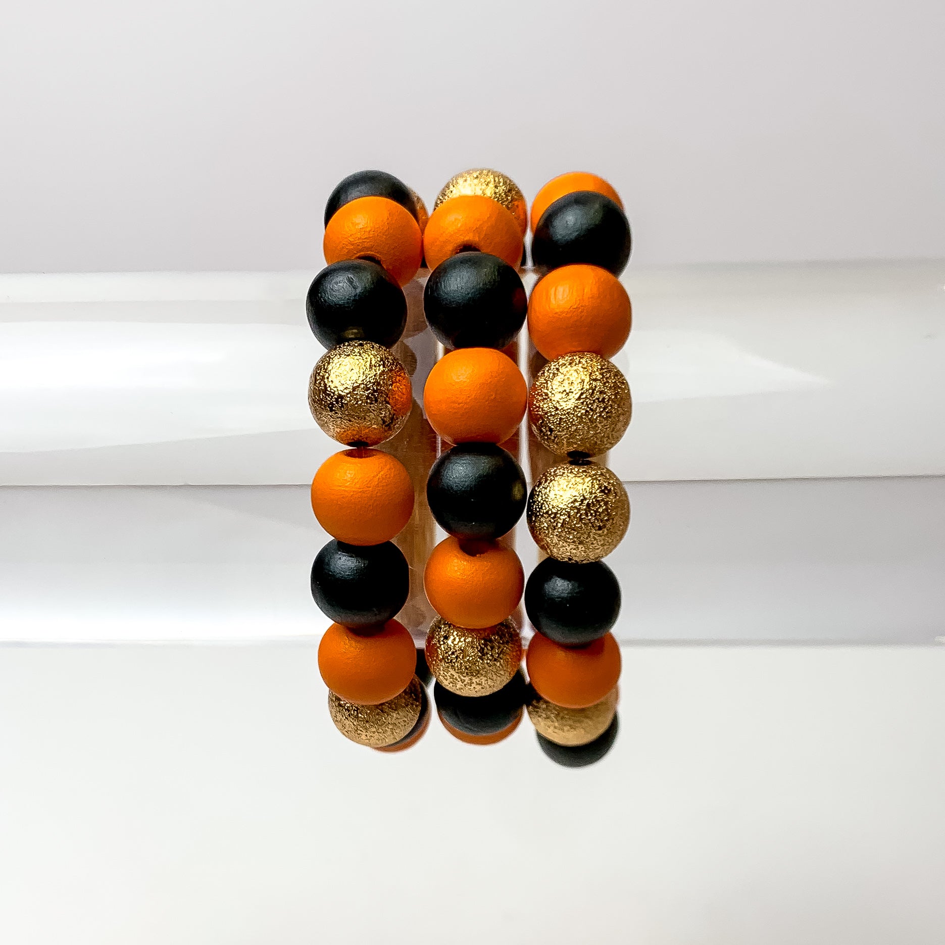 his set of 3 bracelets in the colors orange and black are placed on a clear bracelet display featuring a white background.
