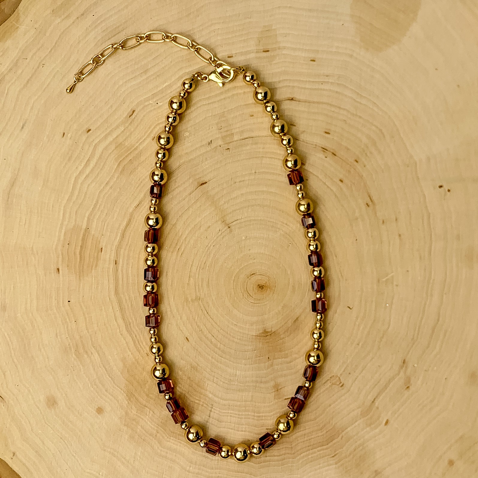 This necklace has gold tone and grape purple beads. It is placed against a wooden background.