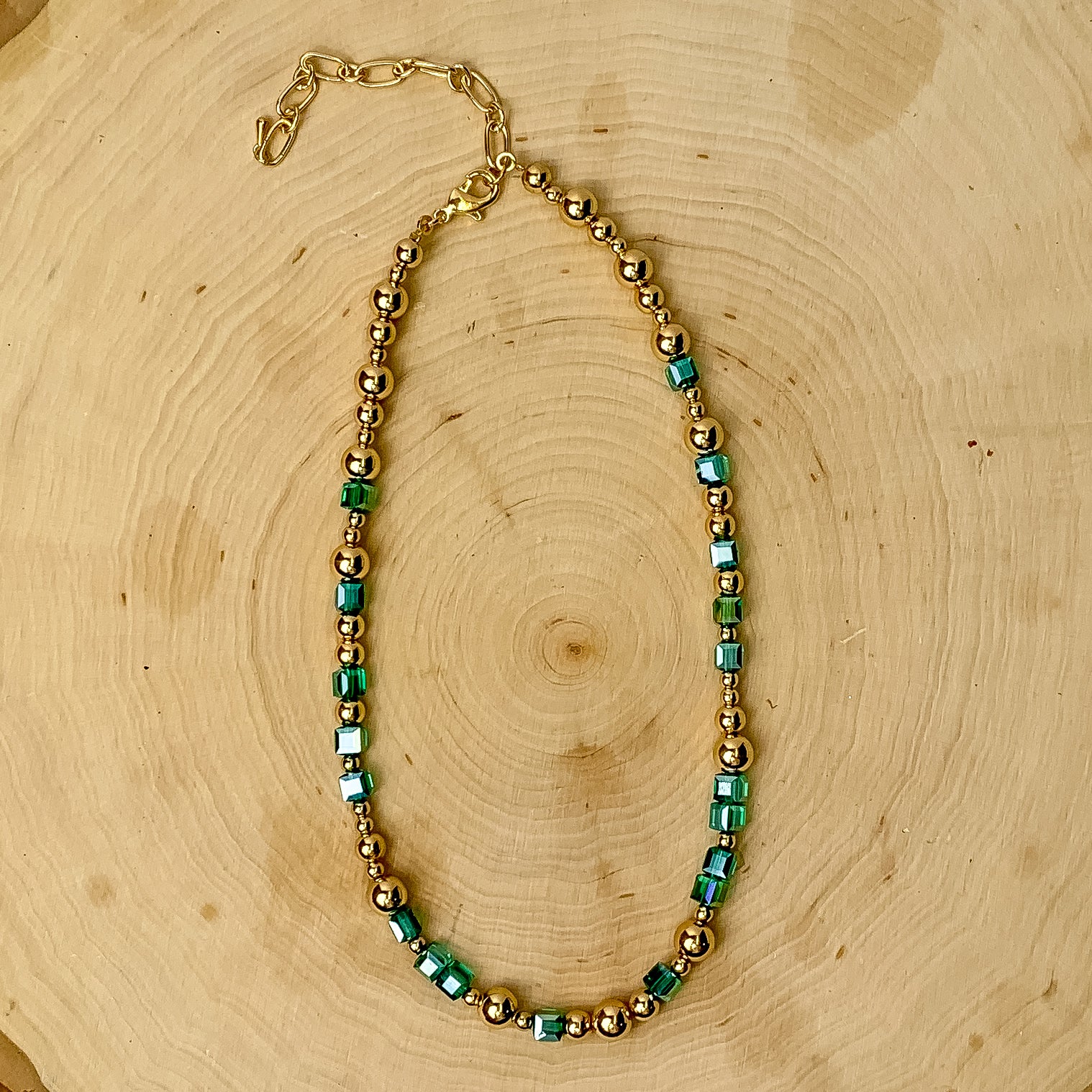 This necklace has gold tone and mint green beads. It is placed against a wooden background.