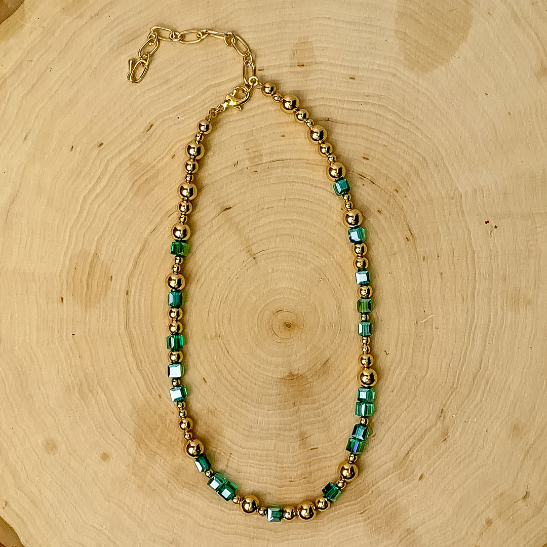 This necklace has gold tone and mint green beads. It is placed against a wooden background.